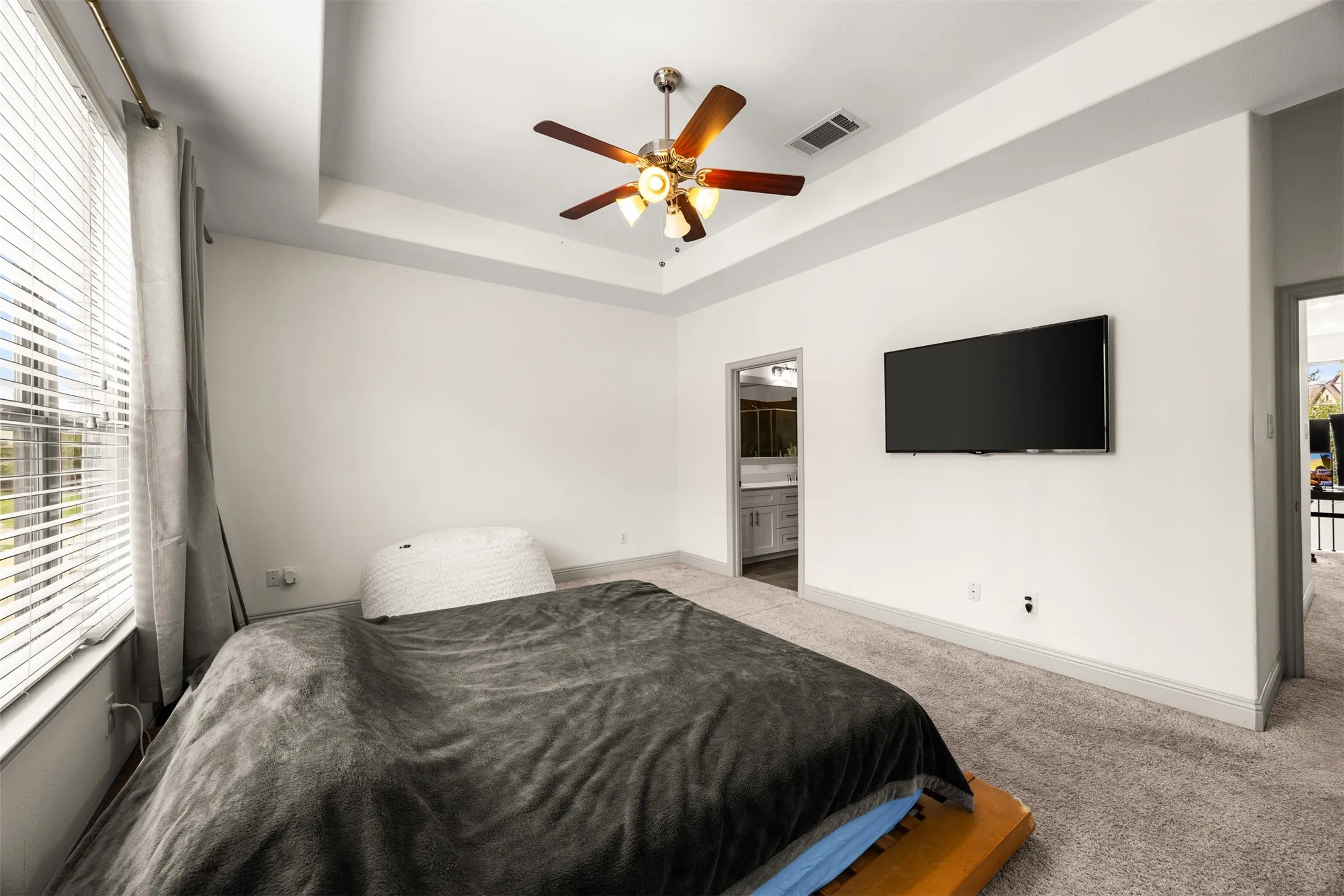Spacious room featuring tray ceilings, neutral carpeting, and a ceiling fan with integrated lighting