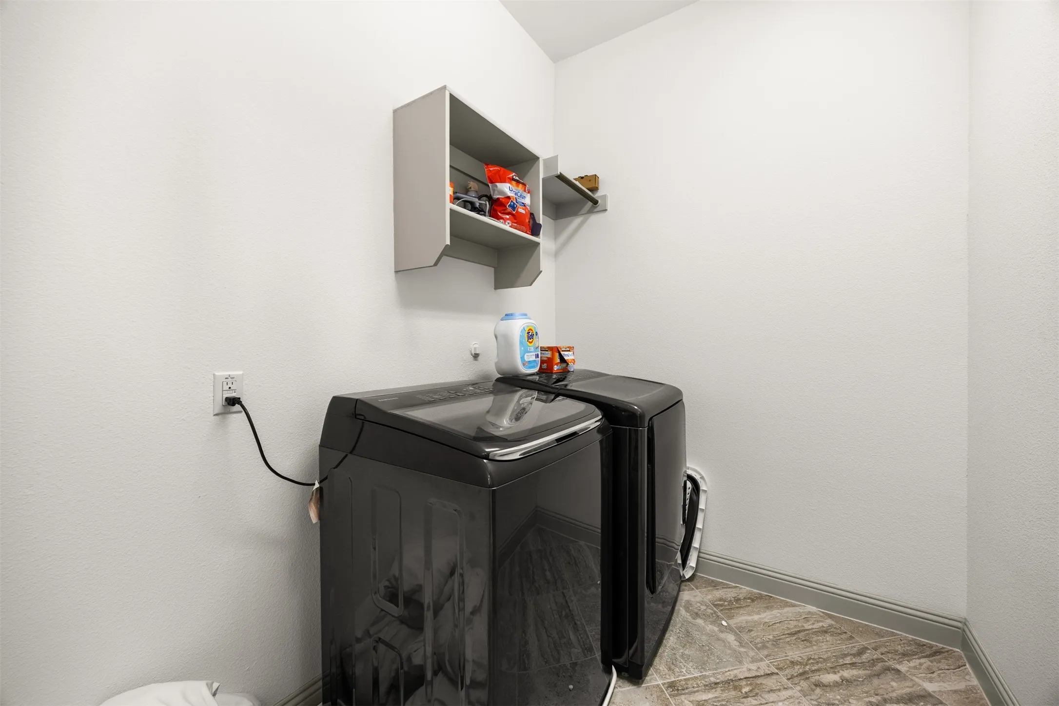 Laundry area featuring a built-in upper shelf, gray baseboard trim, and patterned tile flooring
