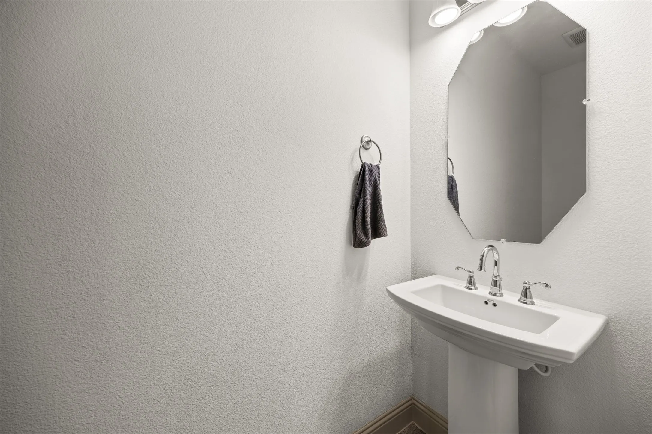 Pedestal sink with chrome fixtures and an octagonal mirror