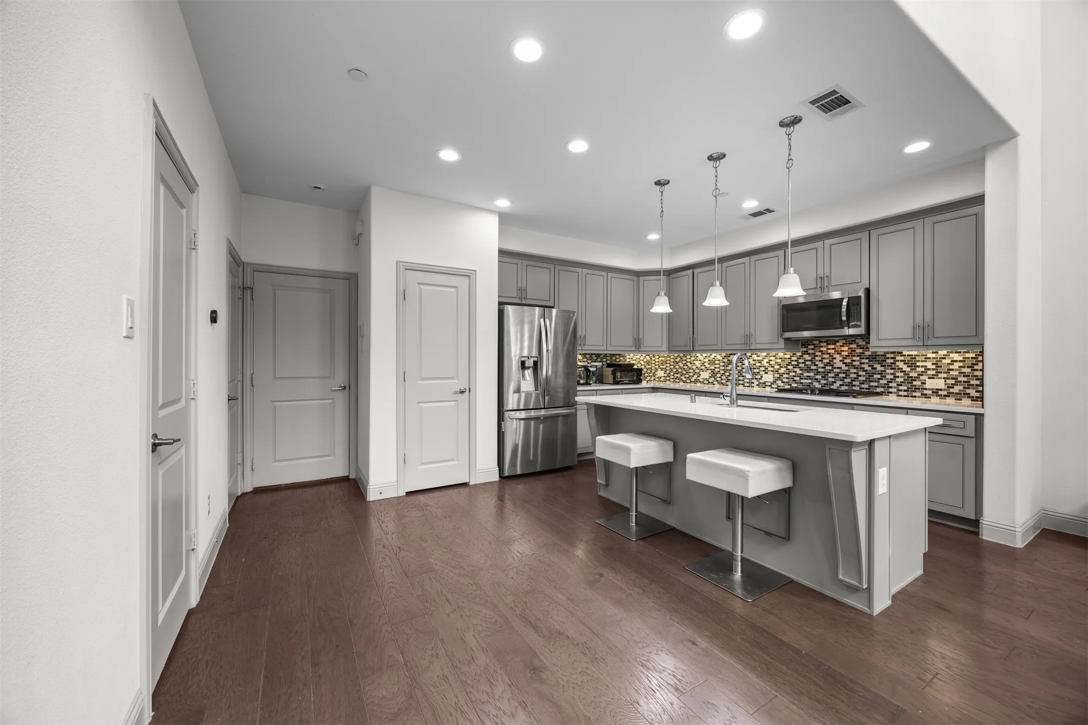Modern kitchen featuring gray cabinetry, stainless steel appliances, a center island with pendant lighting, and a decorative tile backsplash
