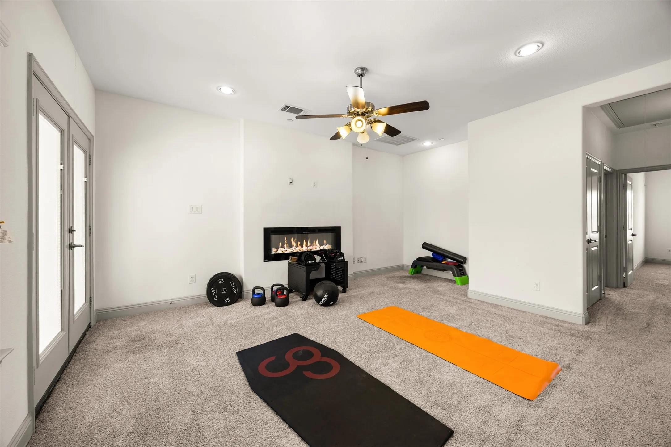 Spacious room featuring light gray carpet flooring, a built-in linear fireplace, a ceiling fan with light fixture, recessed lighting, and double glass-paneled doors