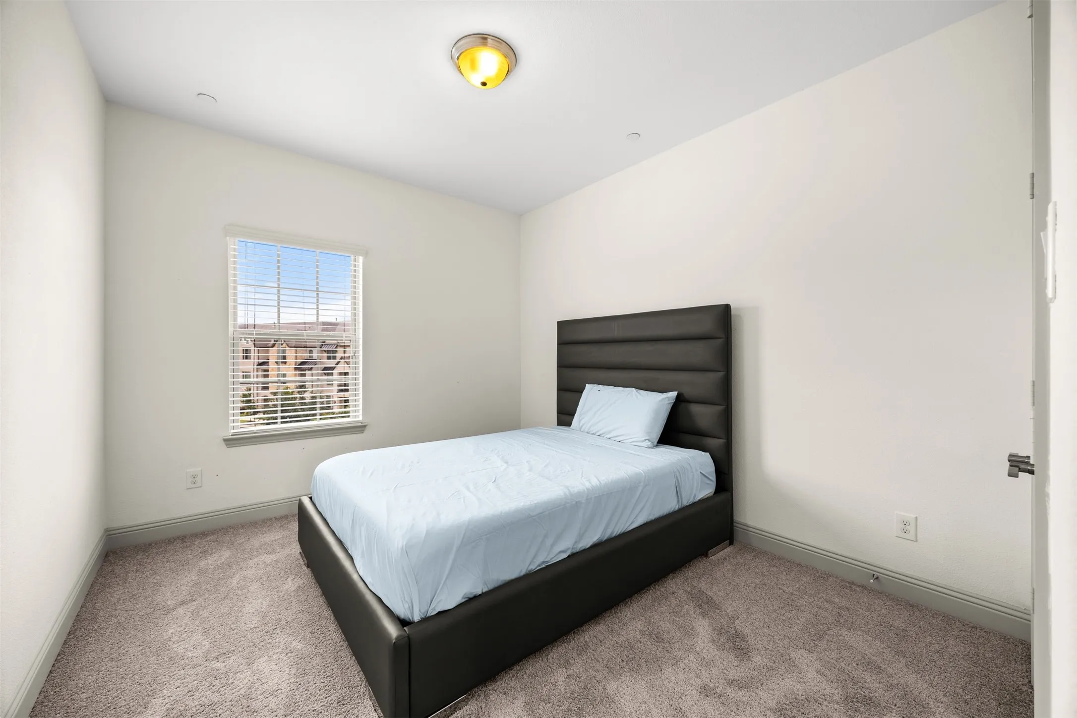 Bedroom featuring neutral wall paint, gray carpet flooring, a single window with blinds, and a flush-mount ceiling light