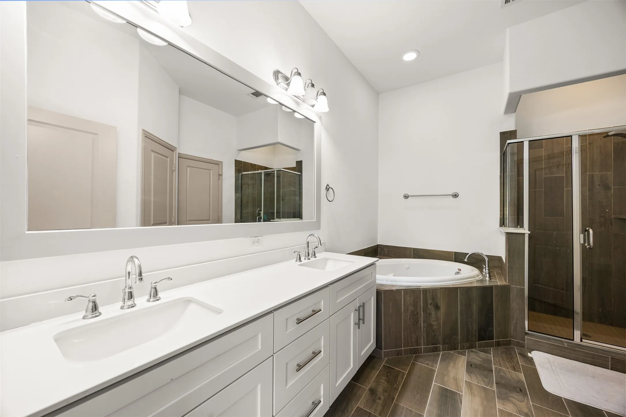 Spacious bathroom featuring a double vanity with white cabinetry and chrome fixtures, a large soaking tub, and a glass-enclosed shower