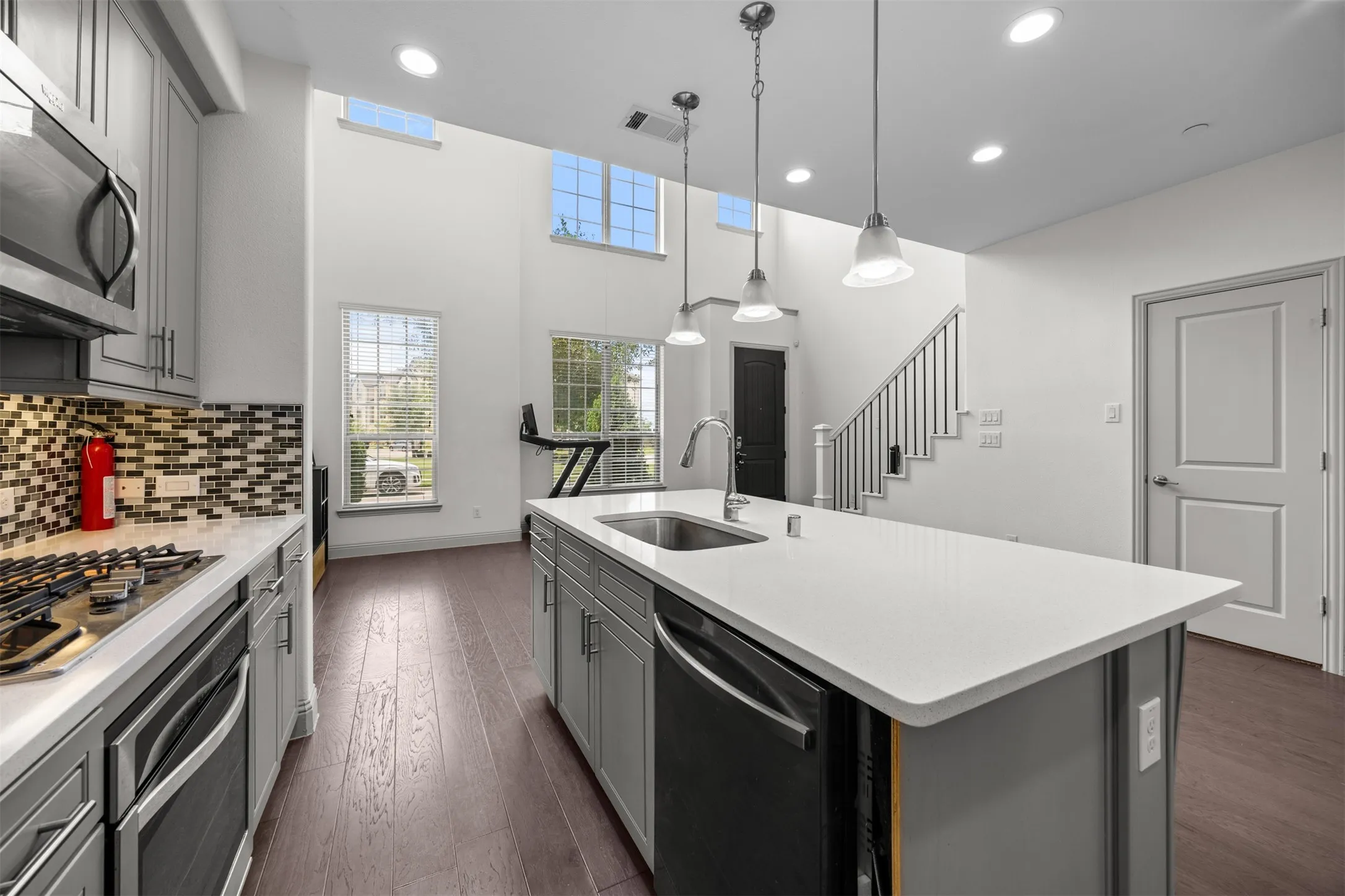 Modern kitchen featuring an island with a stainless steel sink, pendant lighting, and wood-finish flooring