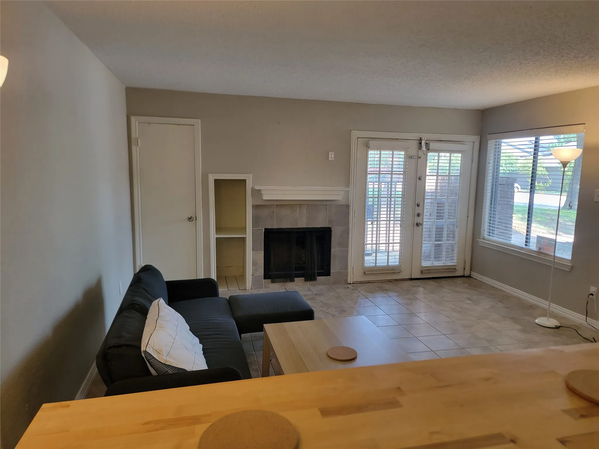 Living area featuring tile flooring, a fireplace with a tiled surround and mantel, built-in shelving, and double glass-paneled doors with blinds