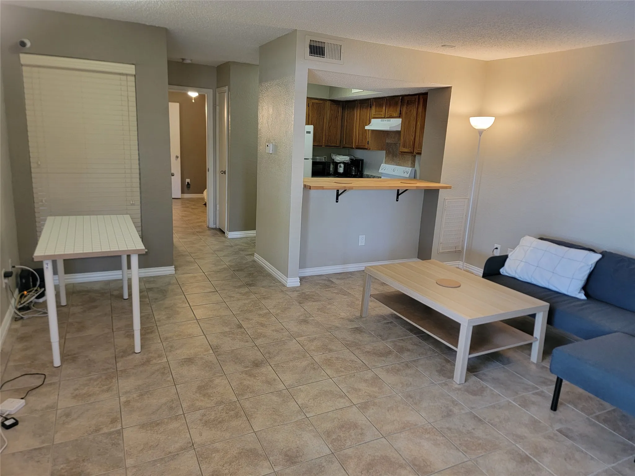 Spacious living area featuring neutral-toned tile flooring, light gray wall paint, and a breakfast bar with a light wood-finish countertop