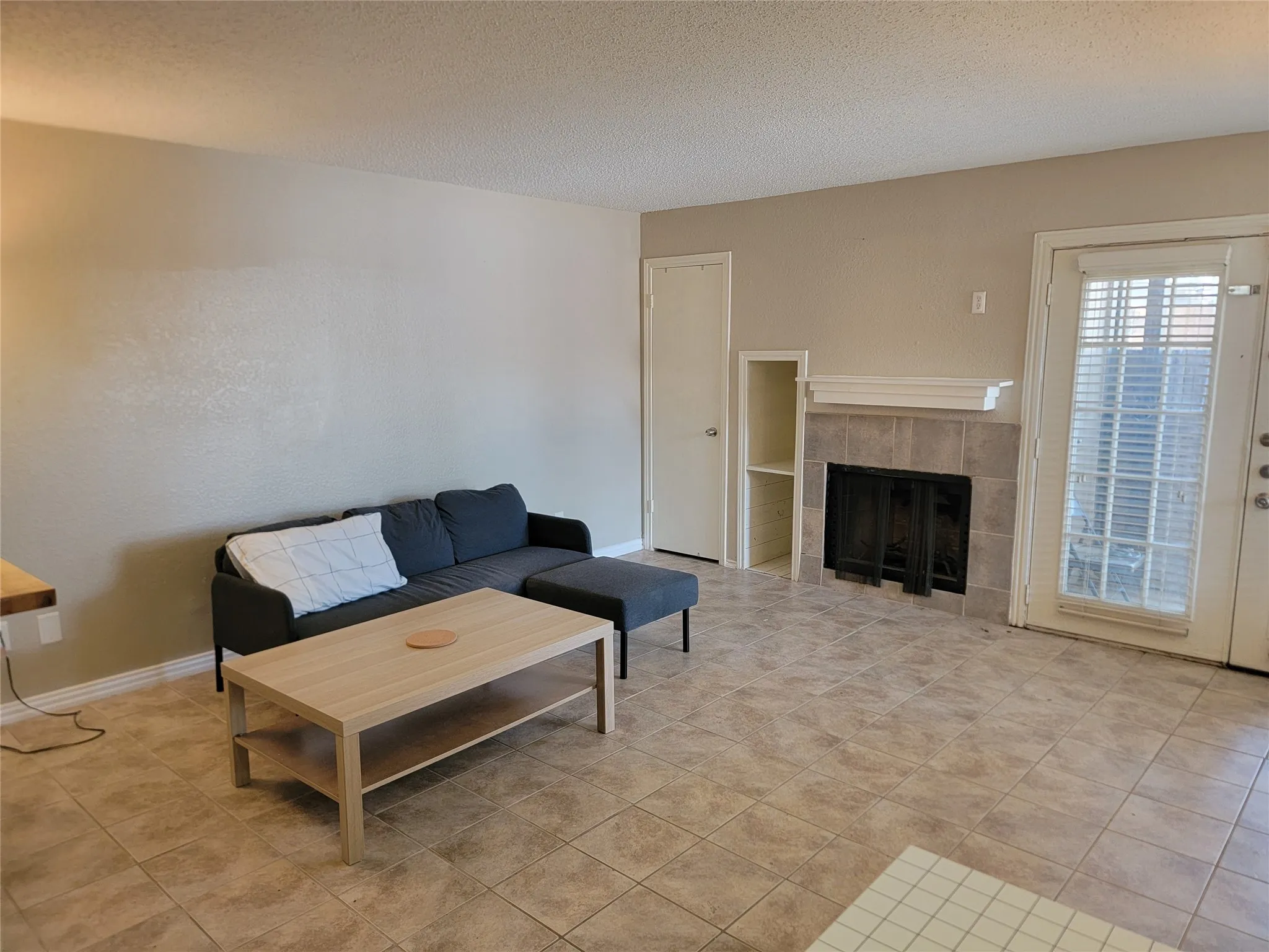 Living area featuring tile flooring, a fireplace with a tile surround and mantel, built-in shelving, and a glass-paned door