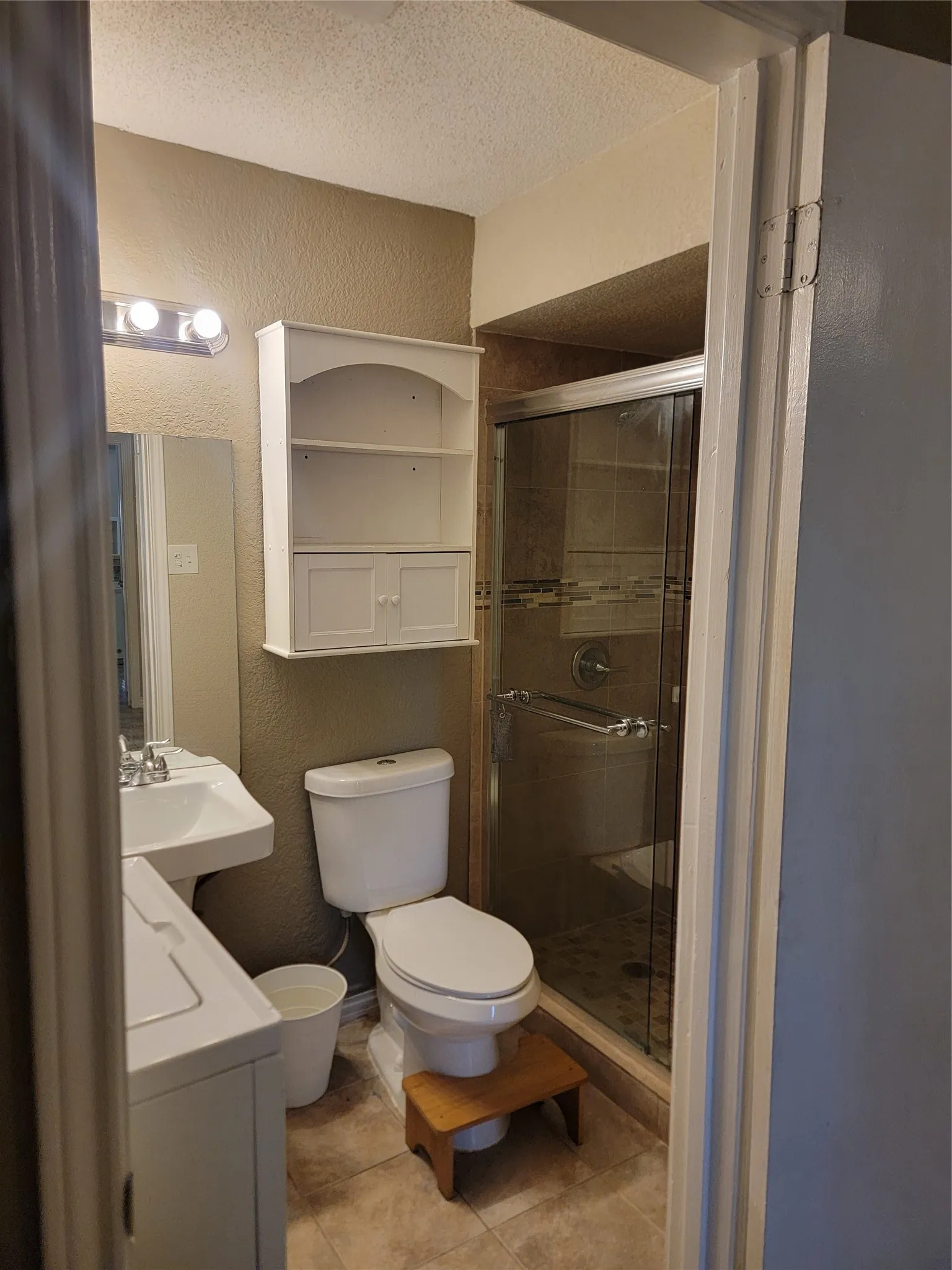 Bathroom featuring a glass-enclosed shower with tile surround, a pedestal sink, and a built-in wall cabinet with open shelving