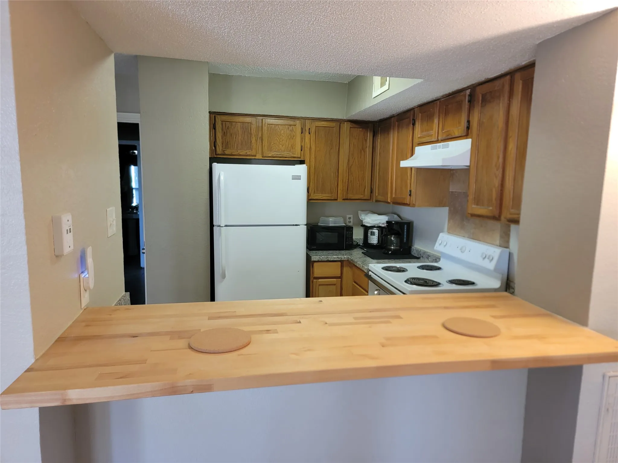 Kitchen with wood-finish cabinetry, white appliances, and a light-toned wood-finish breakfast bar