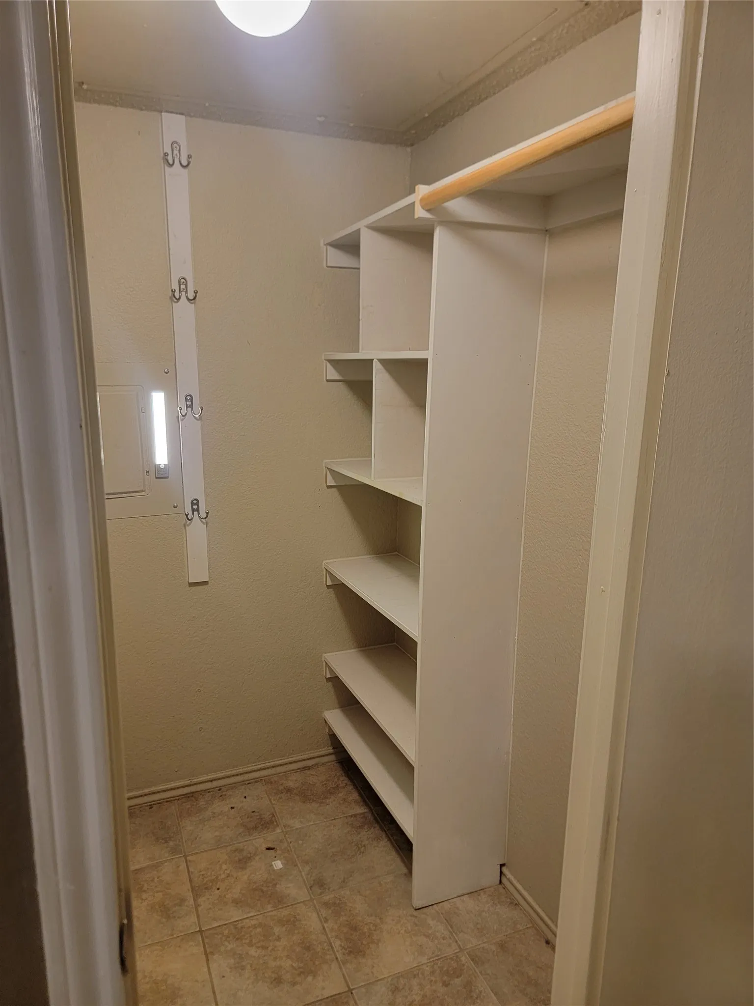 Walk-in closet featuring built-in shelving, a wood-finish hanging rod, wall-mounted hooks, ceiling light fixture, and tile-finish flooring