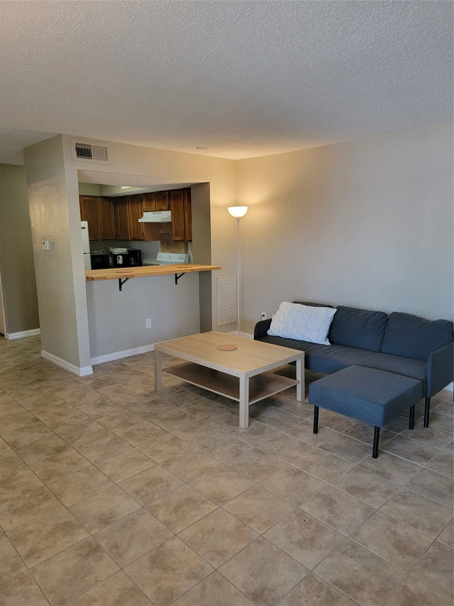 Spacious room featuring tile flooring, light-toned wall paint, and a breakfast bar overlooking the kitchen
