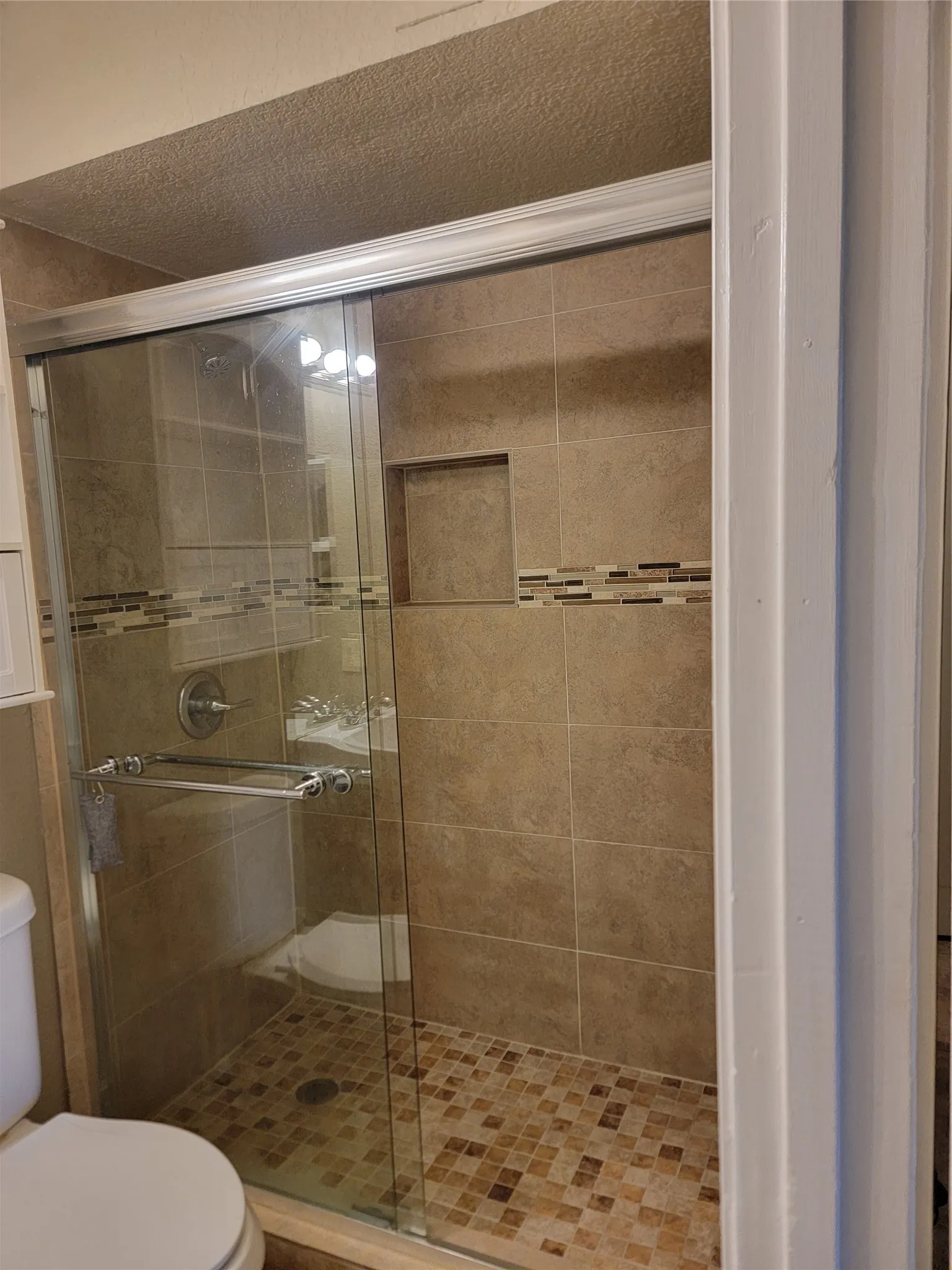 Glass-enclosed shower featuring large format tile walls, a mosaic tile floor, an integrated shower niche, and a chrome shower fixture