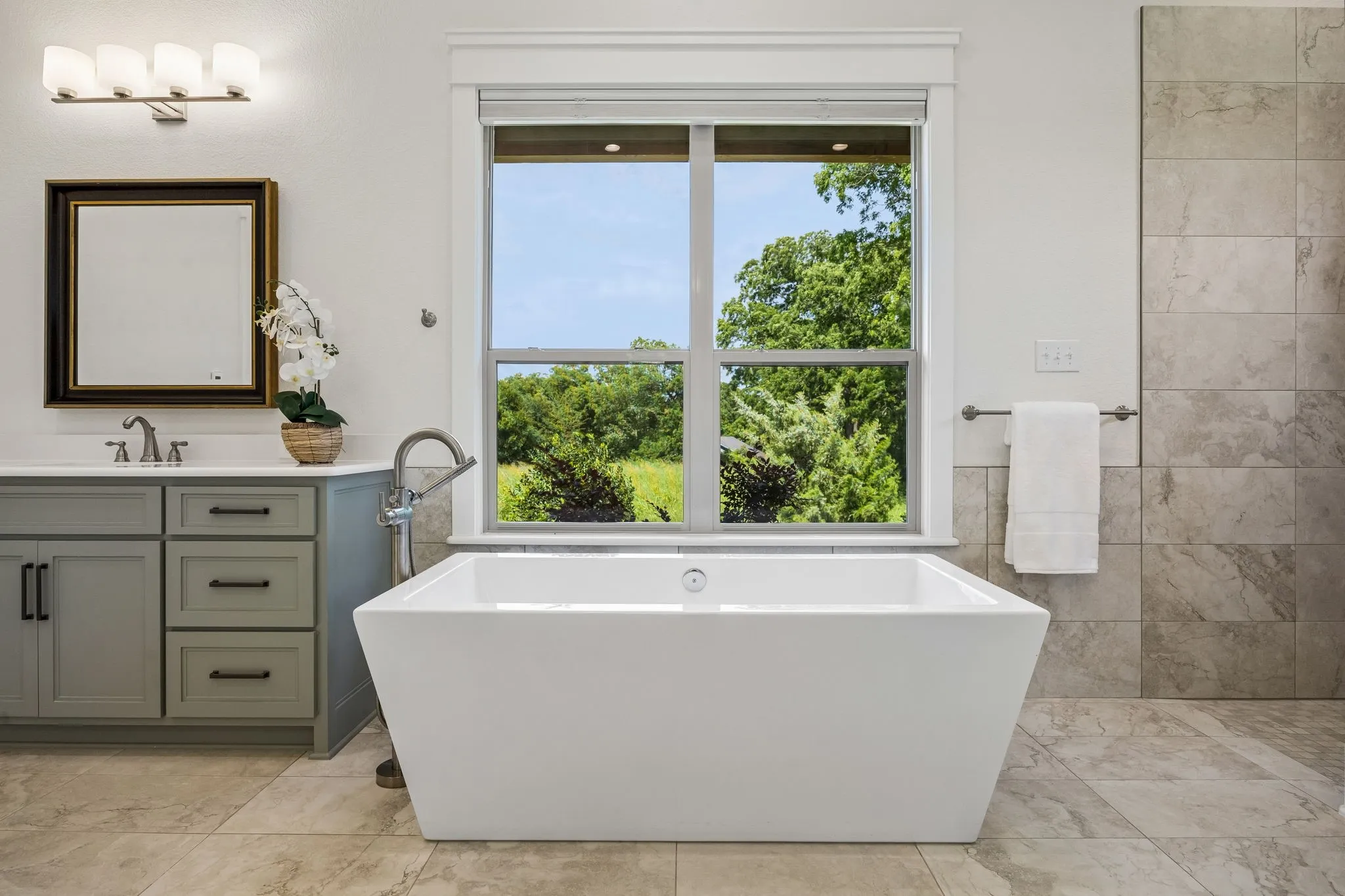 The luxurious primary spa bath features large picture windows, heated tile floors, freestanding soaking tub, large roll-in shower, separate vanities with shaker cabinetry and quartz countertops.