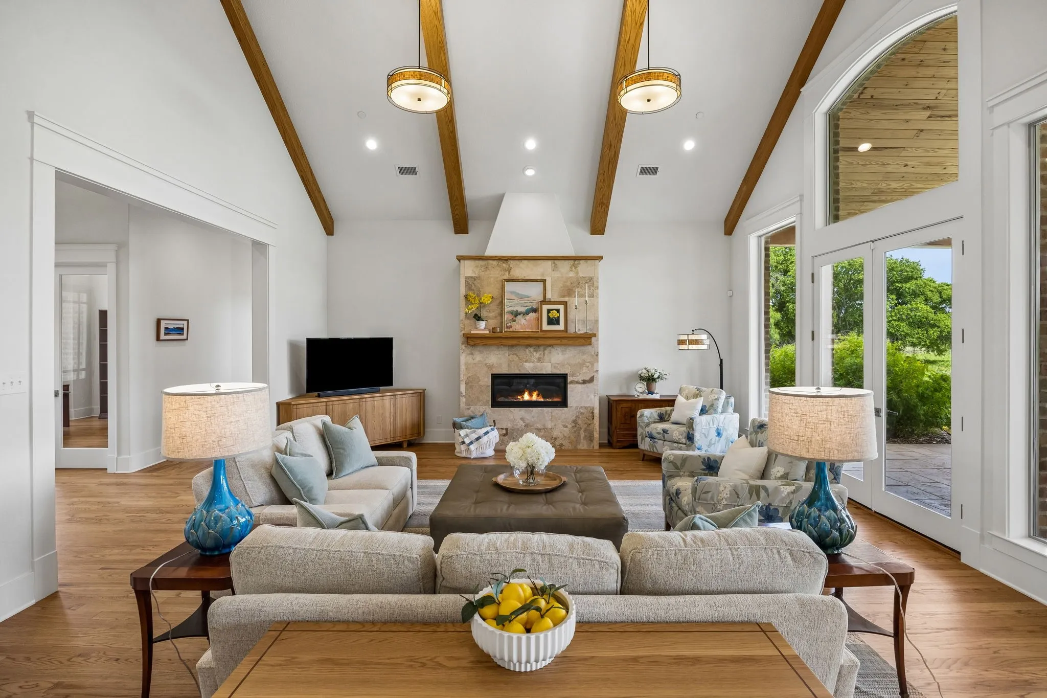 Grand family room with soaring 14-foot ceilings with gorgeous wood beams, fireplace focal, floor-to-ceiling windows, and exterior access to outdoor living.