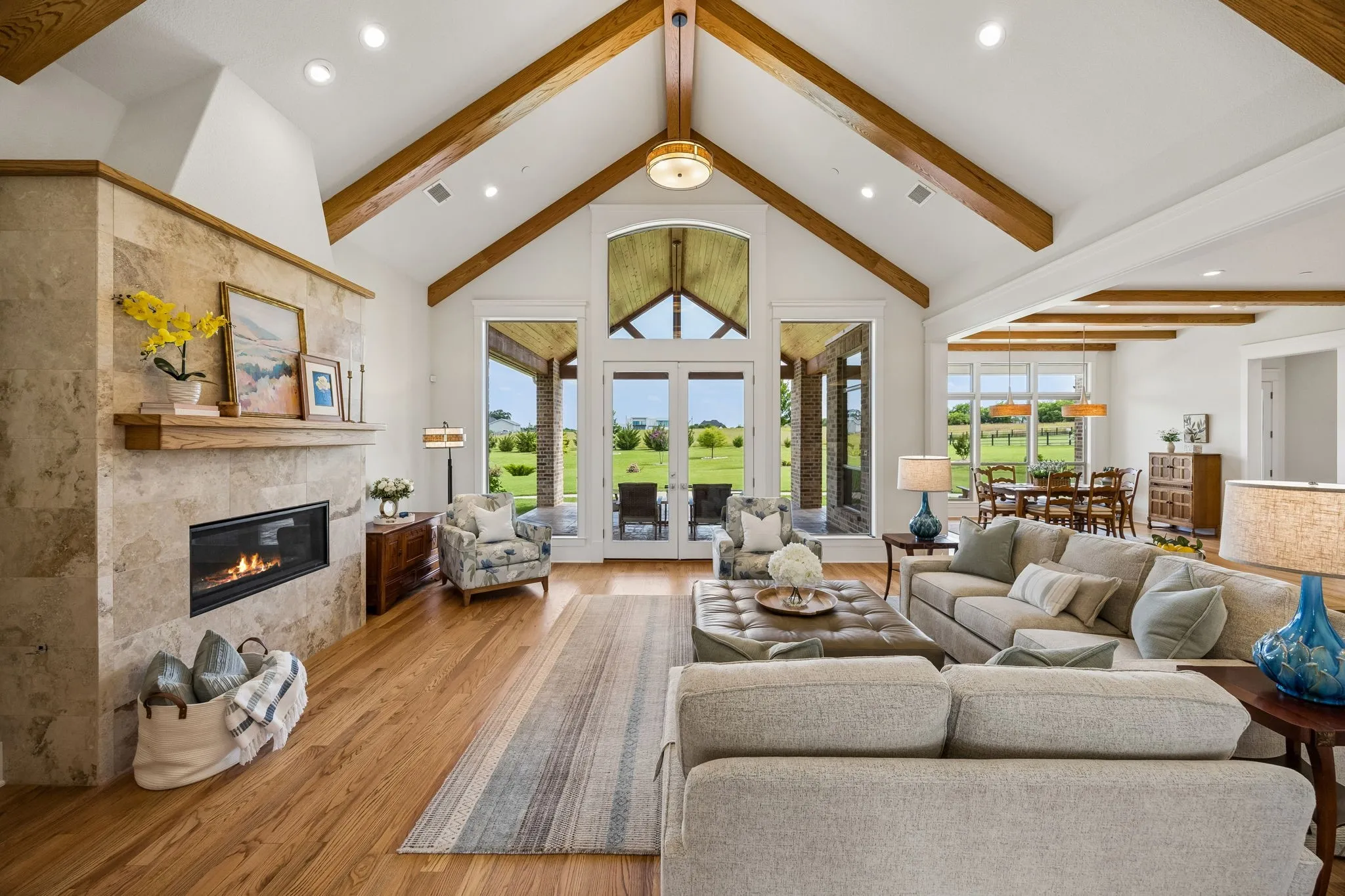Grand family room with soaring 14-foot ceilings with gorgeous wood beams, fireplace focal, floor-to-ceiling windows, and exterior access to outdoor living.