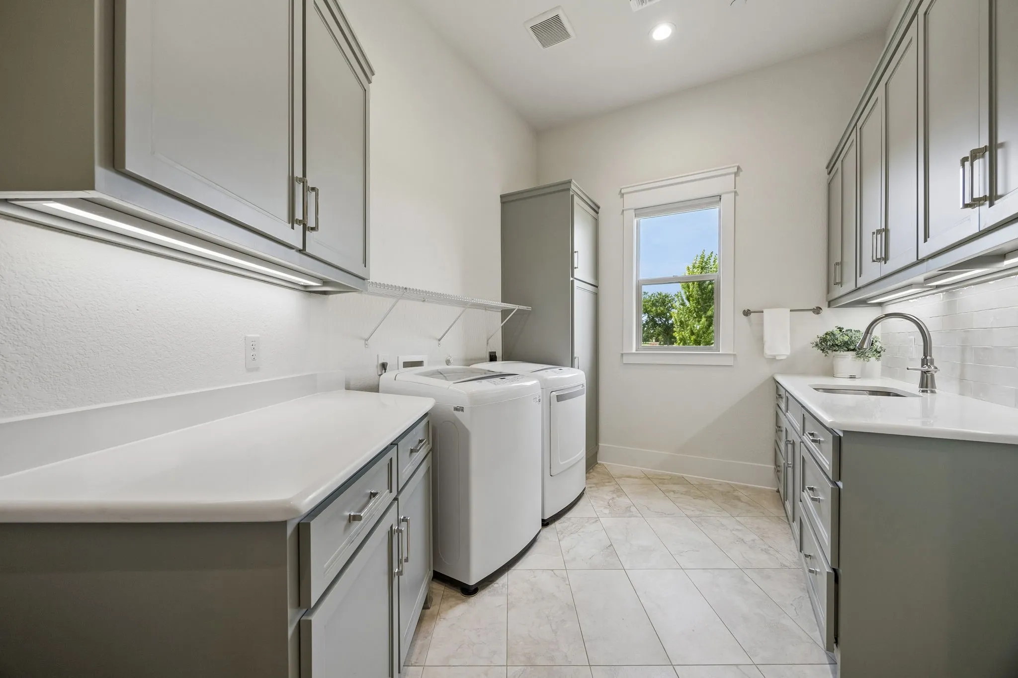Oversized laundry room with mudroom area, undermount sink with gooseneck faucet, extensive cabinetry, and large walk-in storage closet.