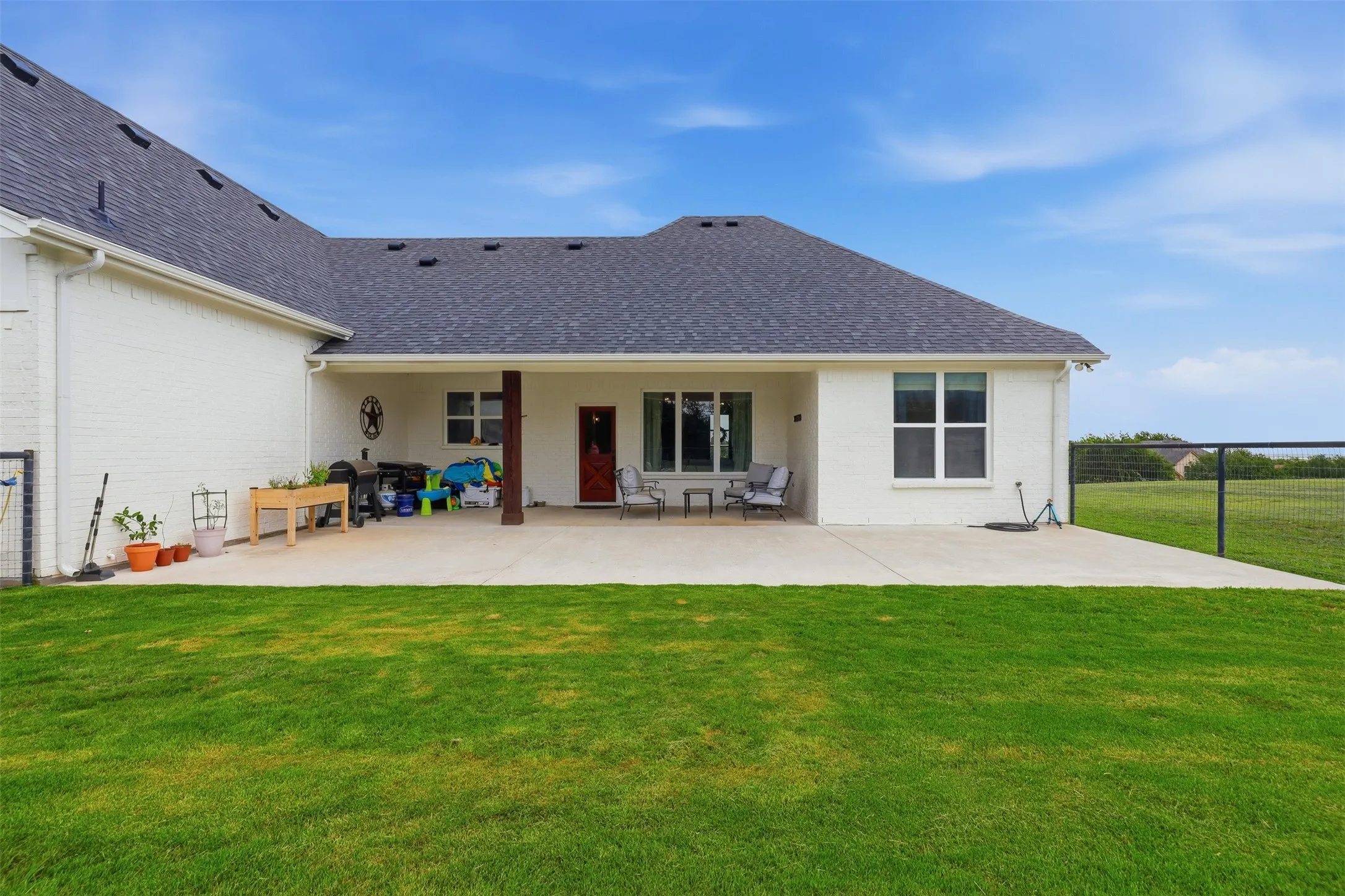 Expansive green lawn with a white brick exterior and a dark shingle roof