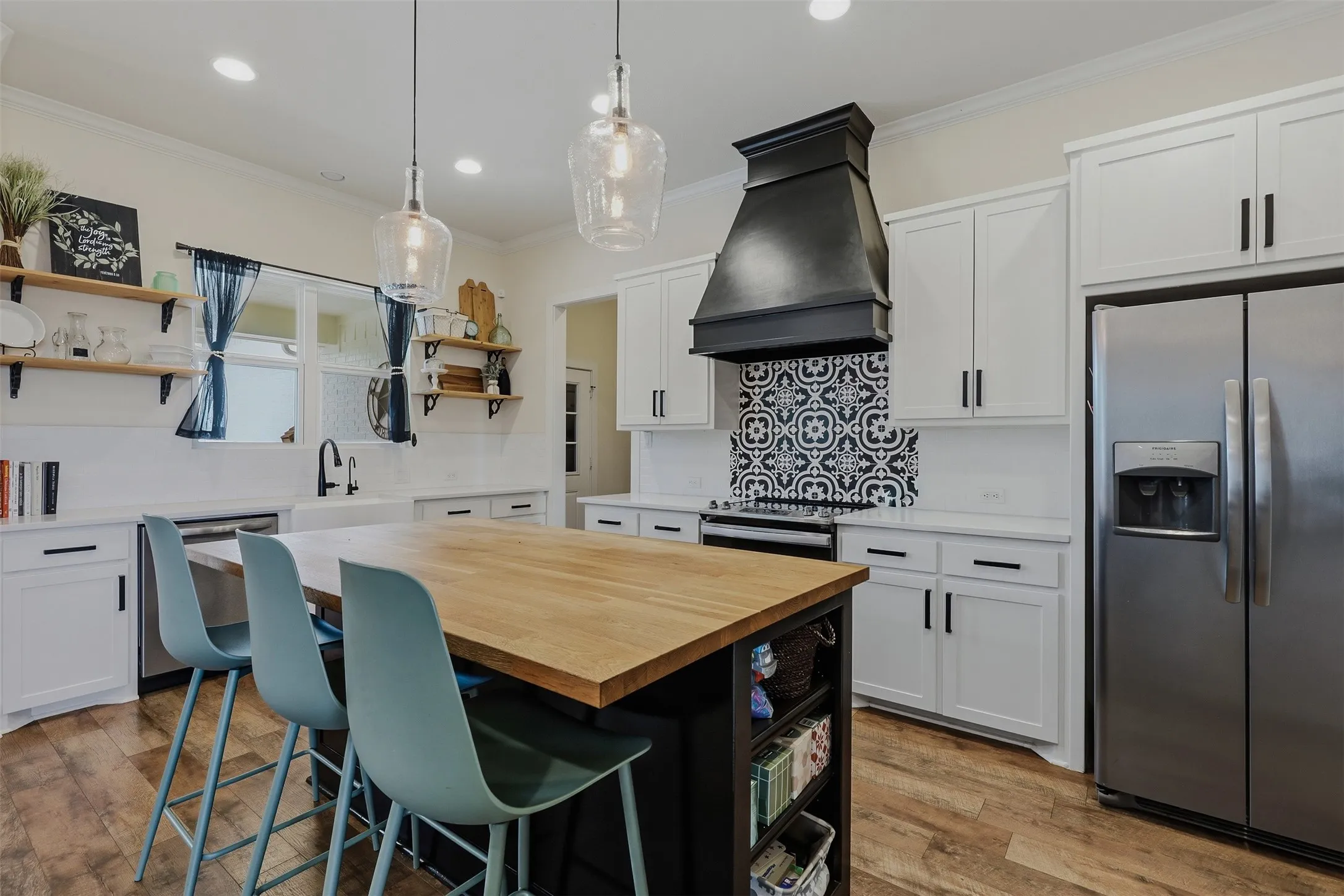 Kitchen featuring a wood-finish island with seating, white shaker cabinetry, stainless steel appliances, and a black and white patterned tile backsplash