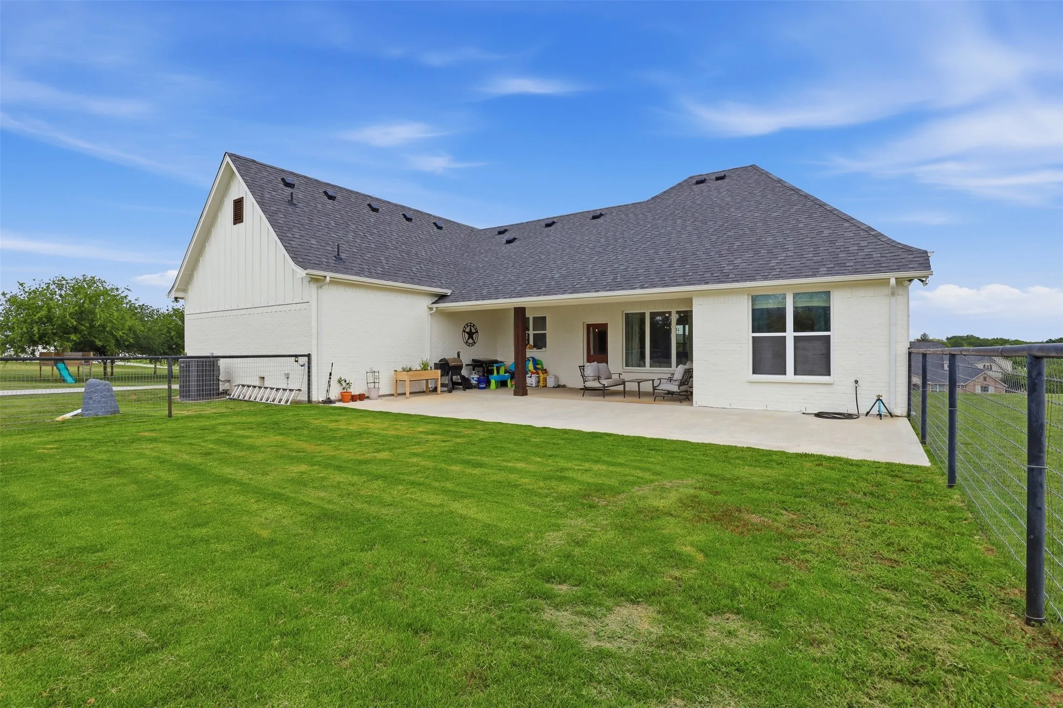 Rear exterior showcasing an expansive lawn, a concrete patio, and a dark shingle roof