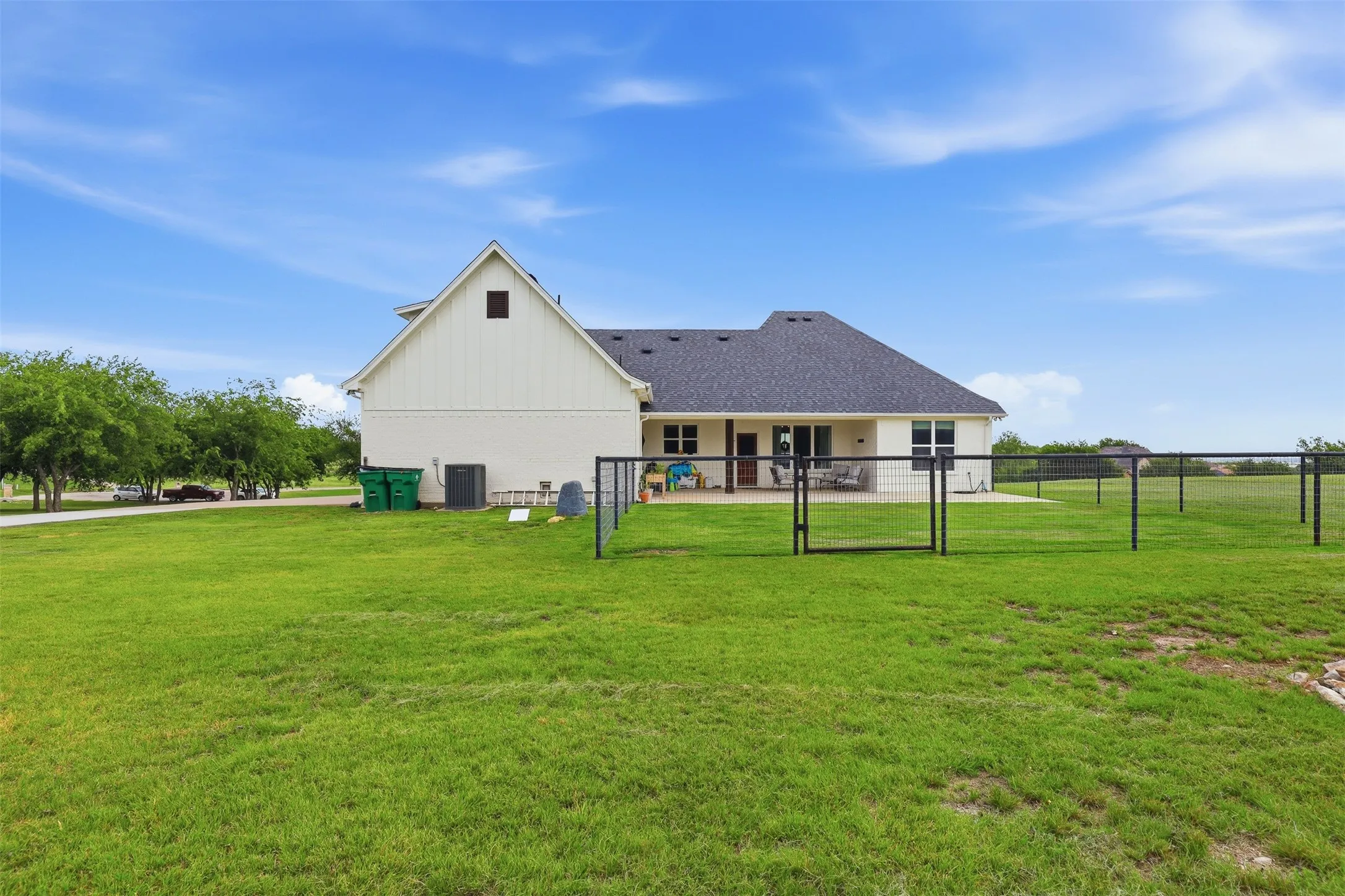 Expansive green lawn surrounds the property, featuring a black metal perimeter fence and a covered rear patio