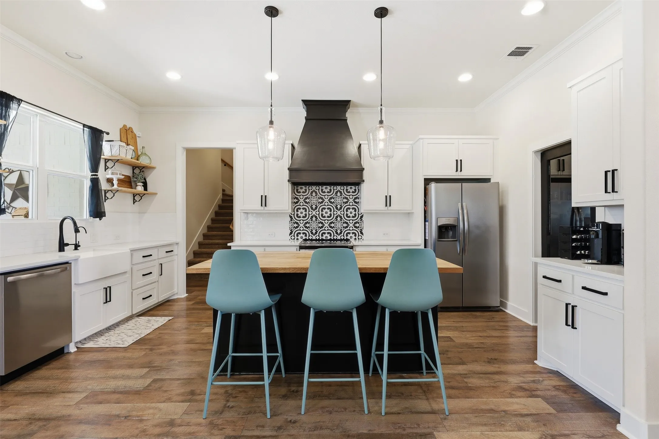 Kitchen featuring wood-finish flooring, an island with a light wood countertop, white shaker-style cabinetry, and a patterned tile backsplash