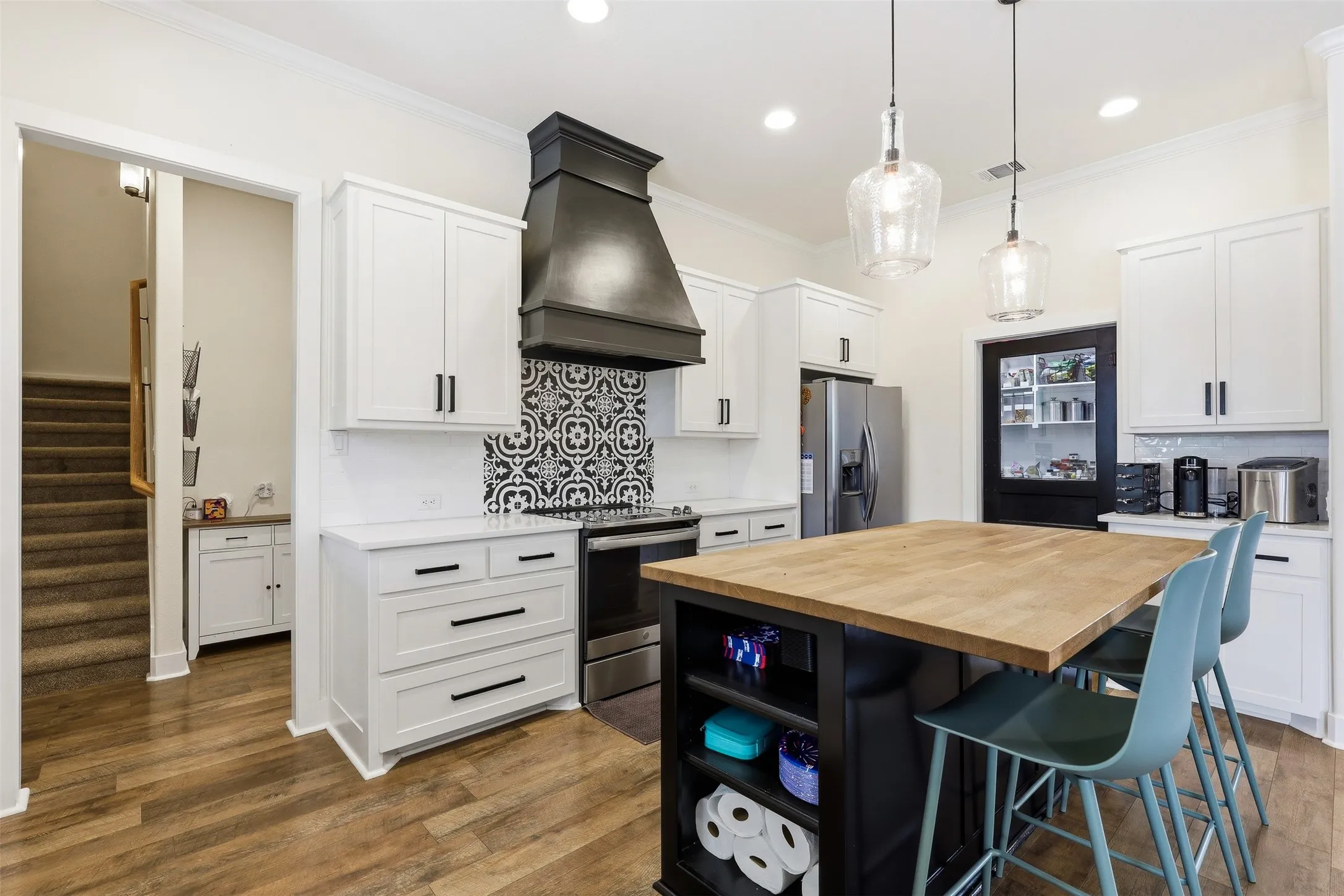Kitchen featuring wood-finish flooring, white cabinetry with dark hardware, a black range hood over patterned tile, and a kitchen island with a wood countertop