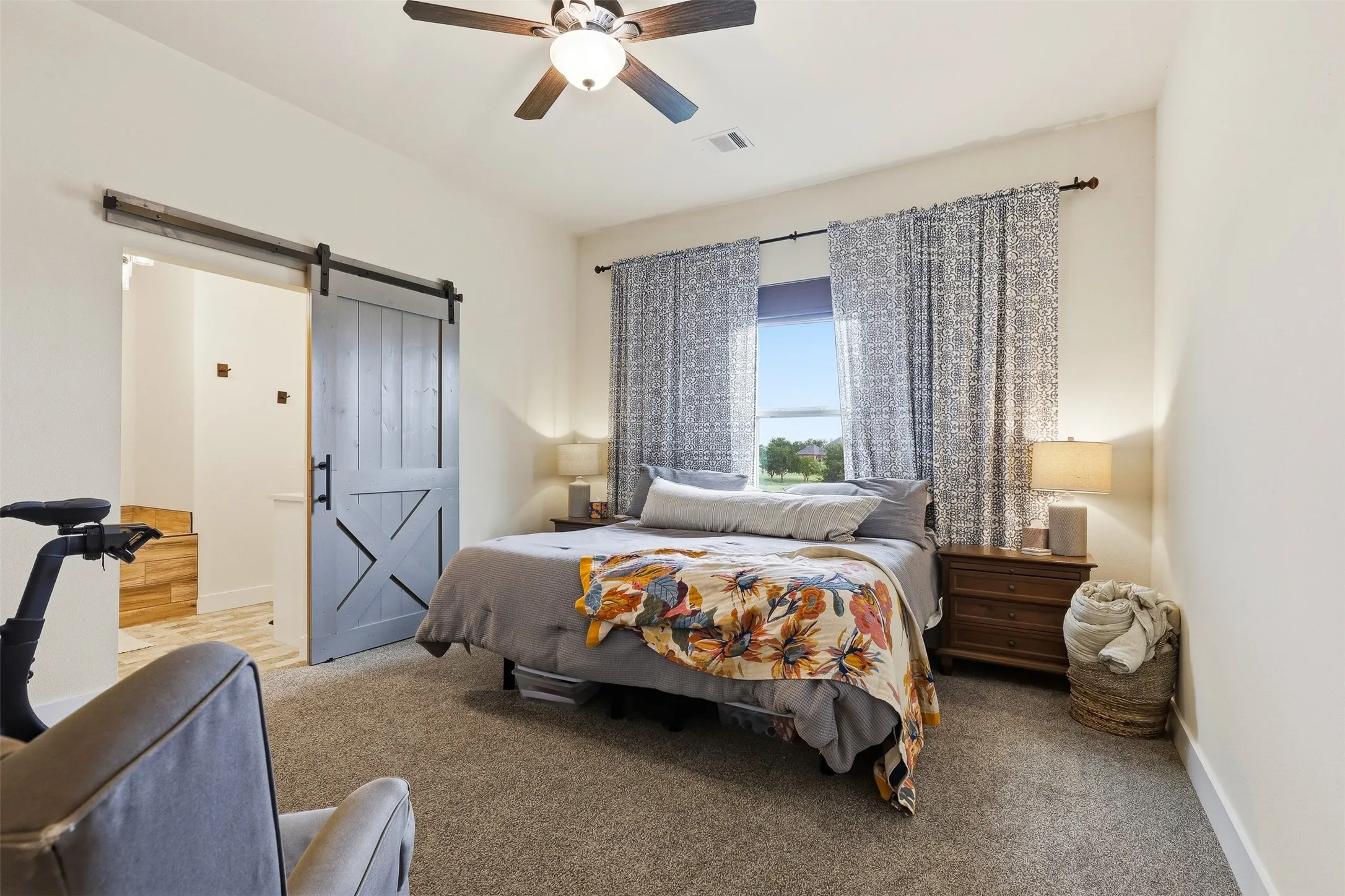 Bedroom featuring a modern farmhouse-style barn door, soft carpet flooring, and a ceiling fan with integrated lighting