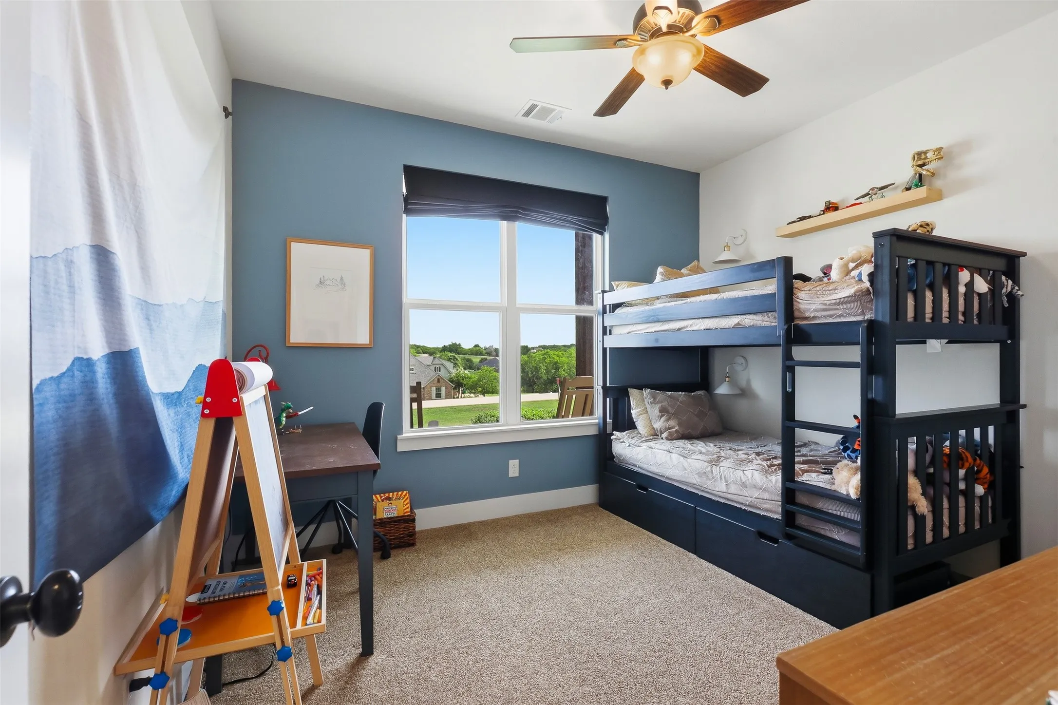 Carpeted room featuring a ceiling fan with light fixture, a window with a roller shade, a built-in bunk bed with integrated storage drawers, and a wall-mounted shelf
