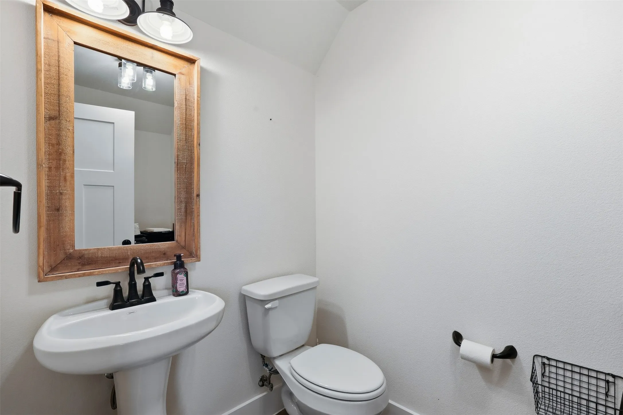 Pedestal sink with matte black faucet under a rustic wood-framed mirror