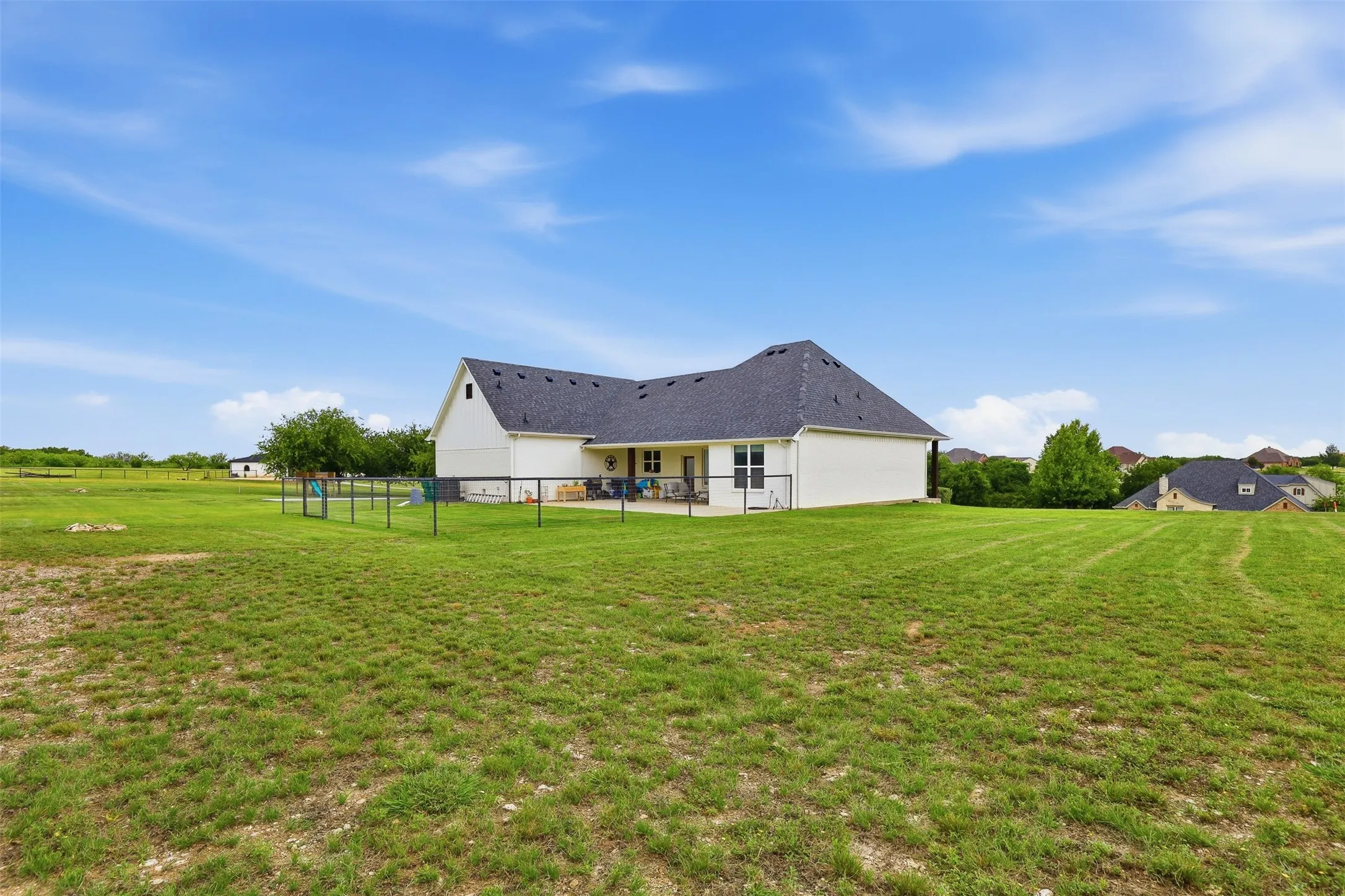 Expansive green lawn bordering a white-sided residence with a dark shingled roof