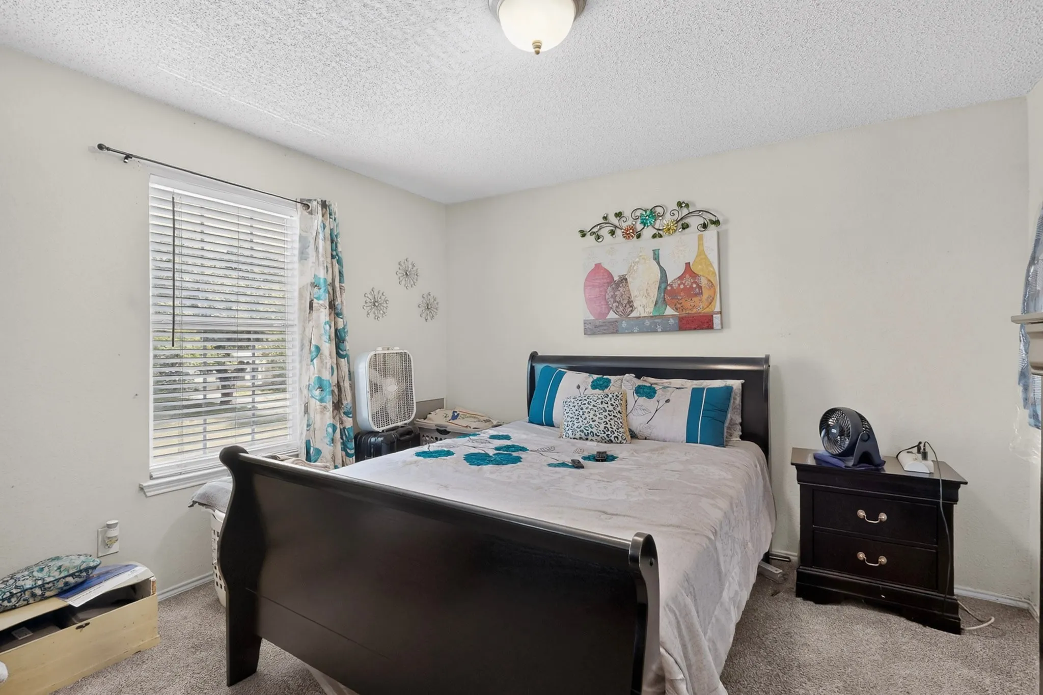 Carpeted room featuring a single window with blinds and patterned curtains