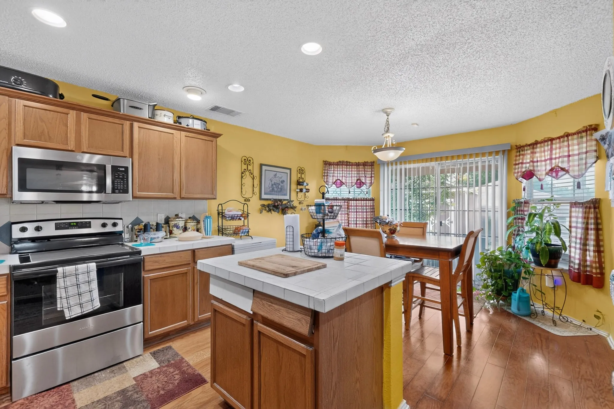 Kitchen featuring wood-finish cabinetry, stainless steel appliances, tiled countertops, recessed lighting, and wood-finish flooring
