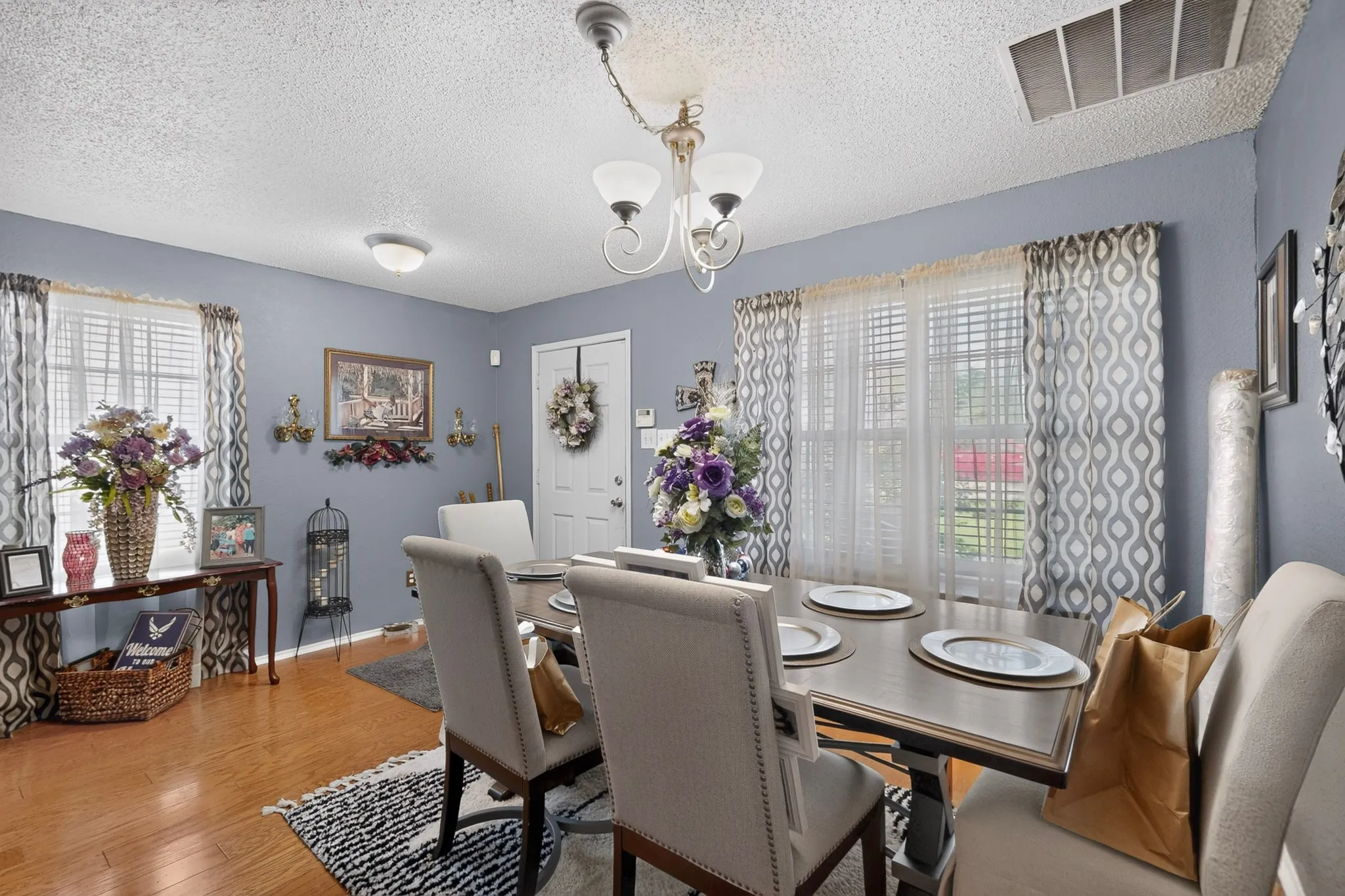 Dining area featuring wood-finish flooring, a white paneled entry door, and multiple windows with blinds