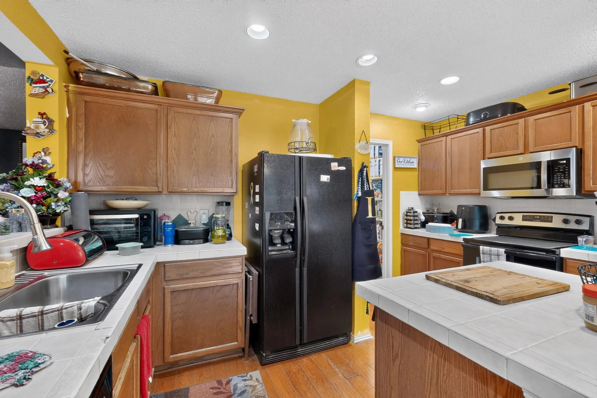 Kitchen featuring wood-finish cabinetry, tile countertops, recessed lighting, and a stainless steel microwave