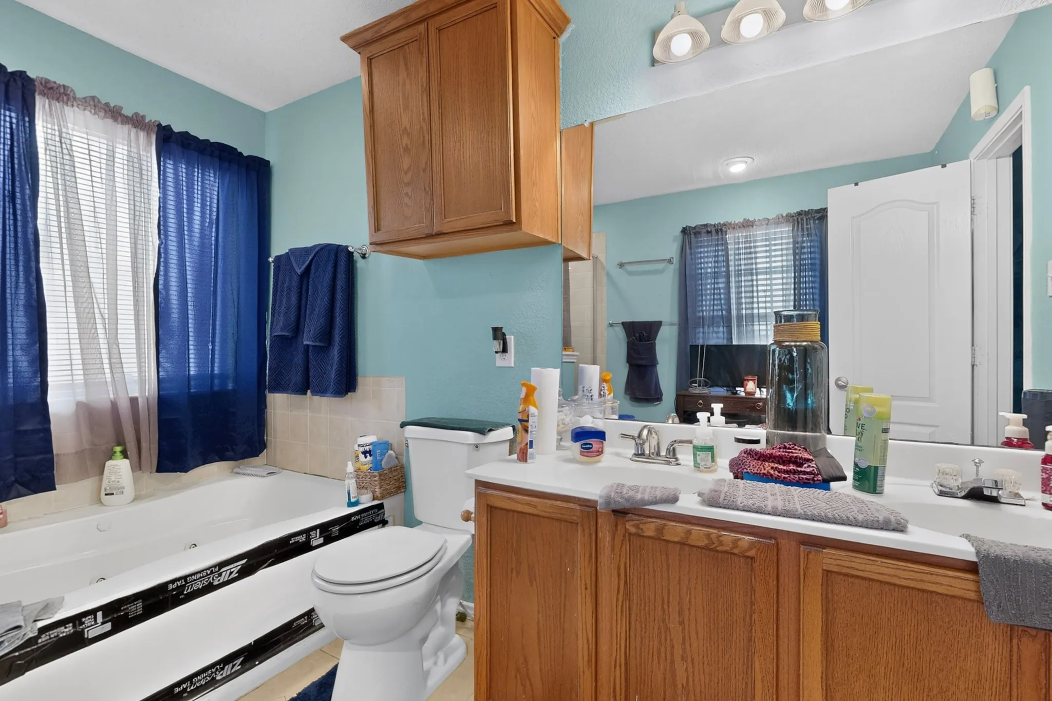 Bathroom featuring a built-in tub, white toilet, vanity with light wood-finish cabinetry, and an overhead light fixture