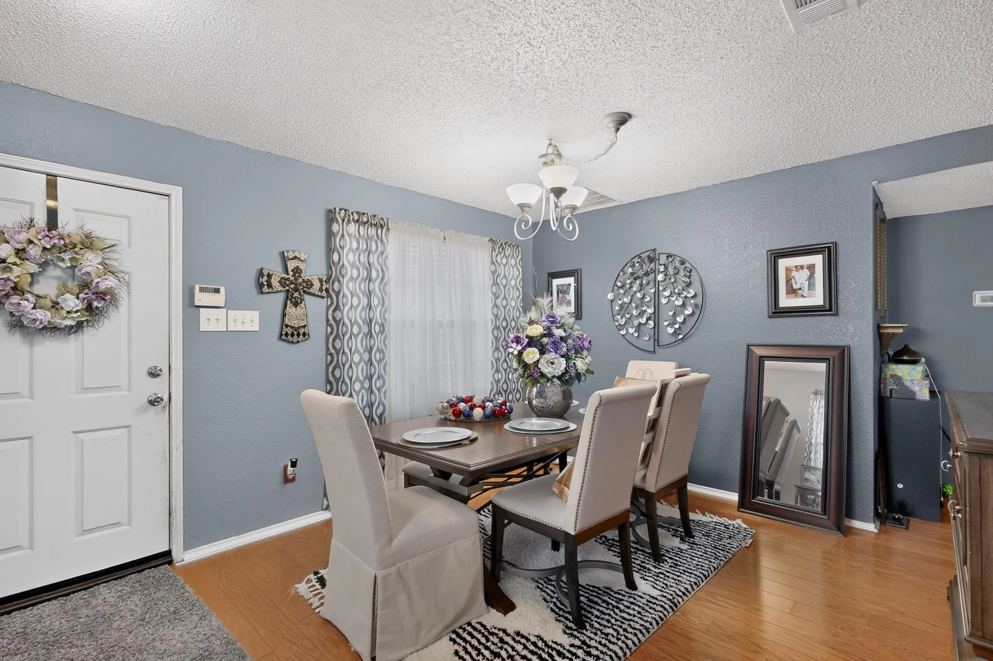 Dining area featuring wood-finish flooring, a contemporary chandelier, and a large window with patterned curtains