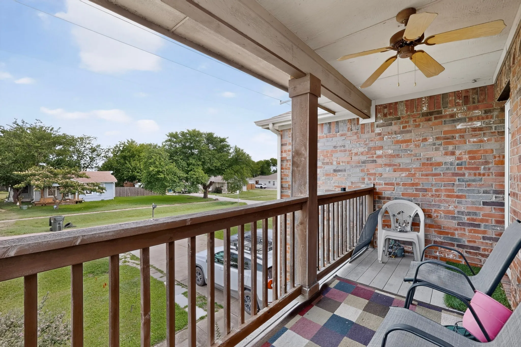 Covered porch featuring a ceiling fan, brick wall, wood-finish railing, and composite decking
