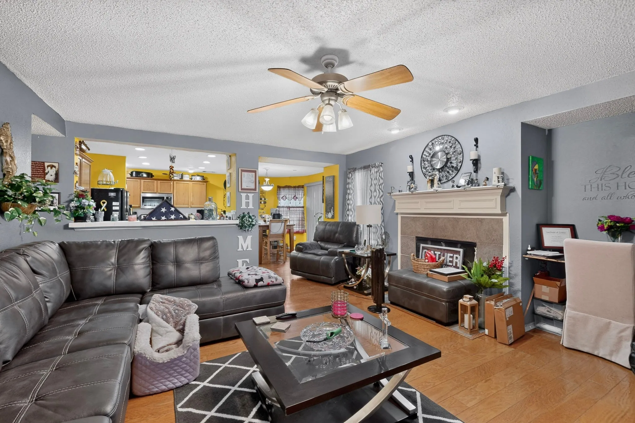 Living area featuring wood-finish flooring, a ceiling fan with integrated lighting, and a fireplace with a white mantel and stone surround