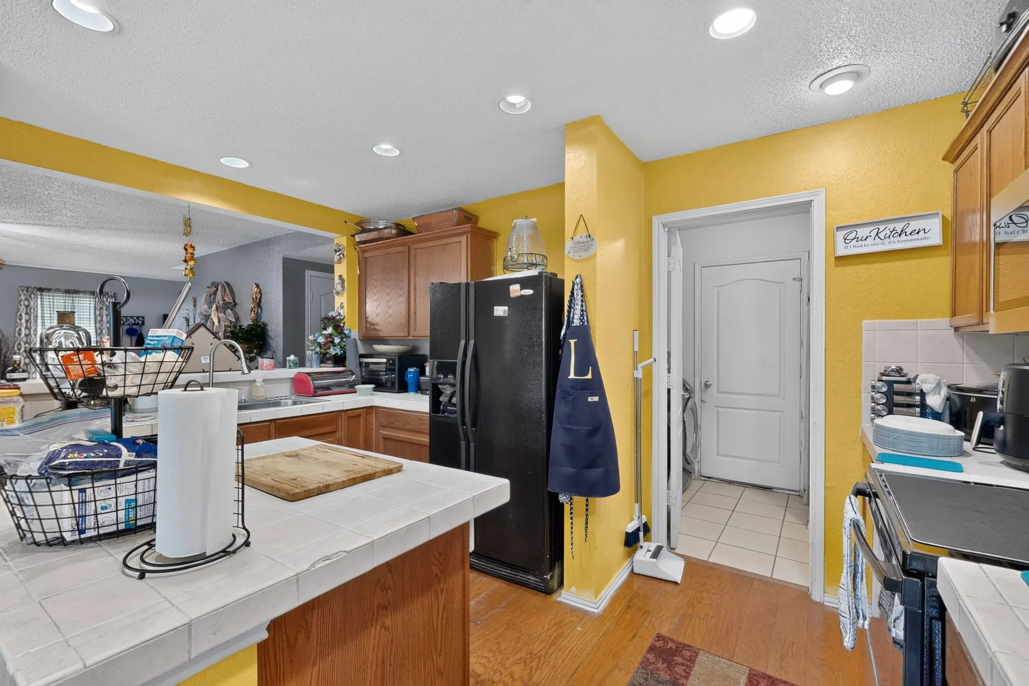 Kitchen with wood-finish flooring, recessed lighting, and a partial wall opening to an additional room
