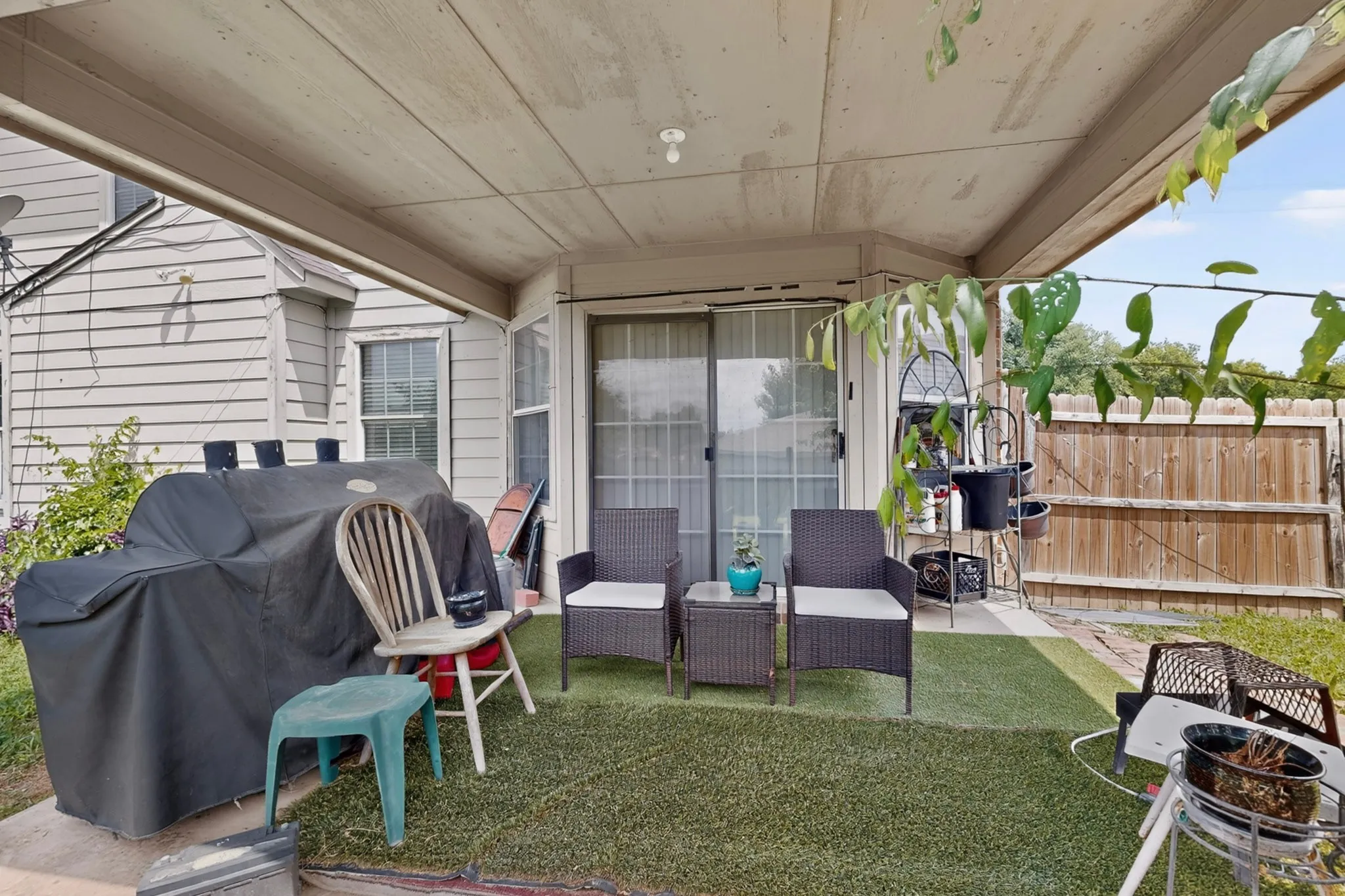 Covered patio area featuring a sliding glass door, artificial turf flooring, and a privacy fence