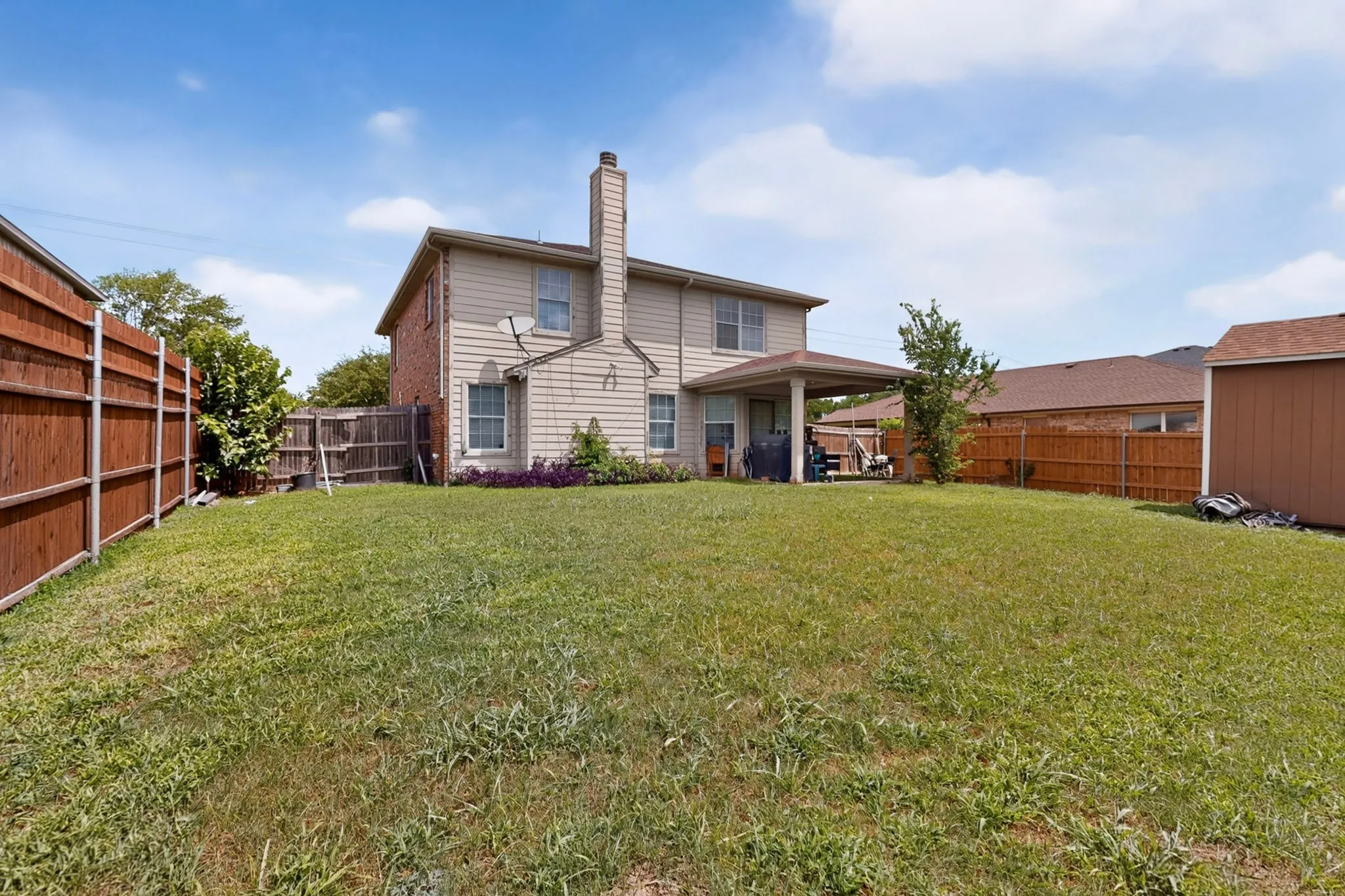 Spacious backyard featuring a covered patio, extensive lawn, wood privacy fencing, and a detached storage shed
