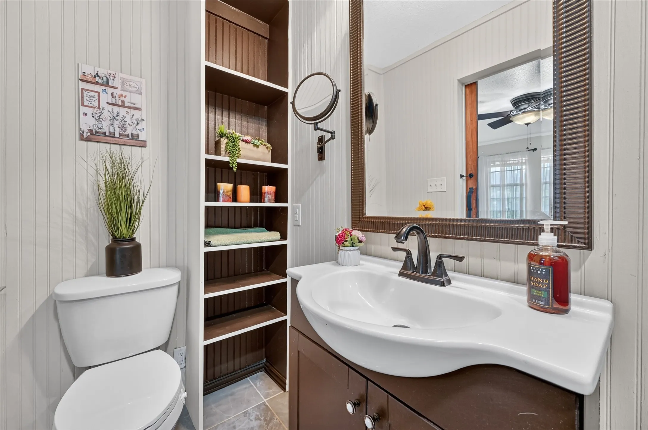 Bathroom featuring beadboard wall panels, a dark wood-finish vanity with an integrated sink, a dark-framed mirror, and built-in shelving