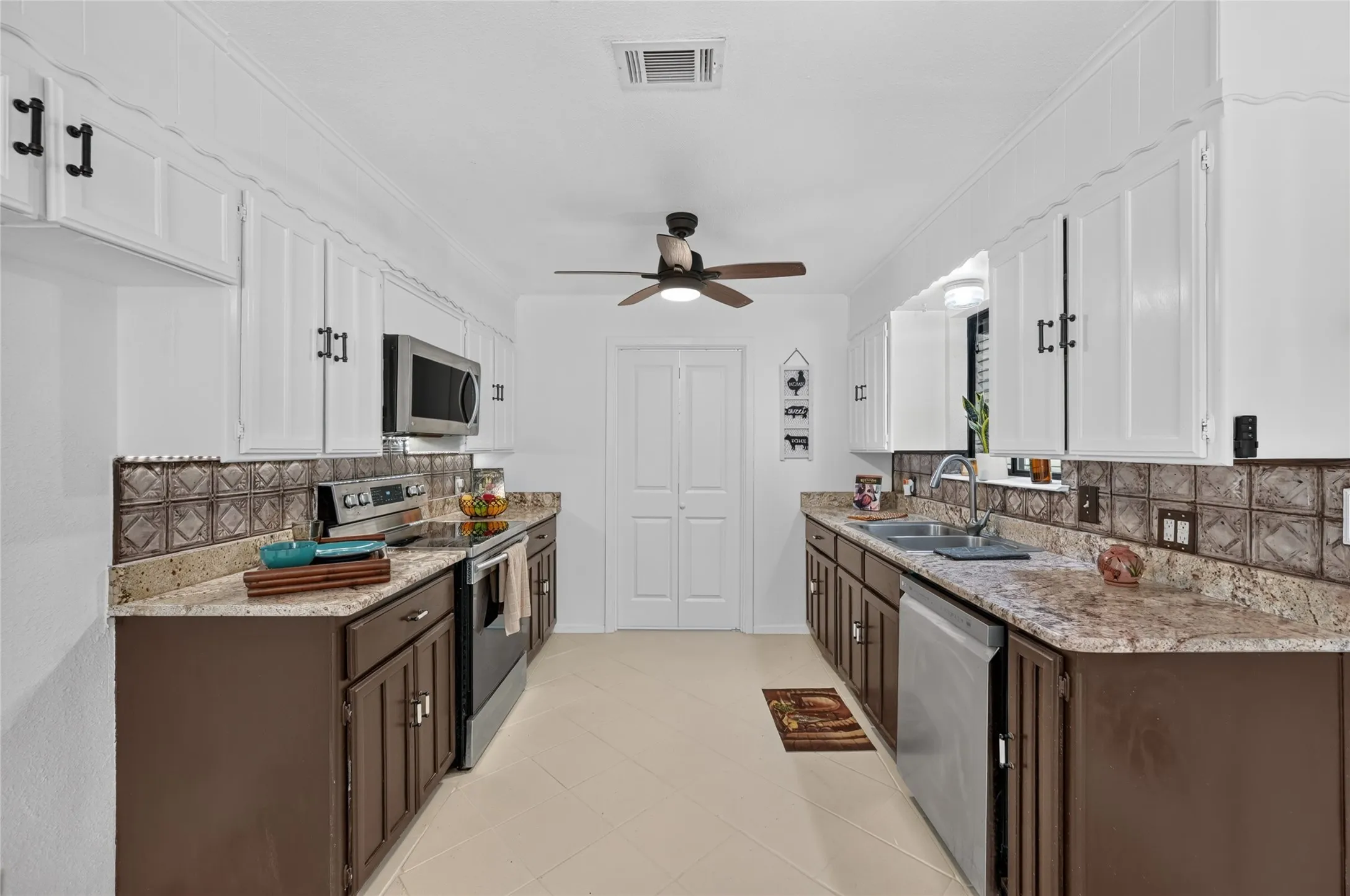 Galley kitchen featuring dual-tone cabinetry, stainless steel appliances, granite countertops, and a decorative tile backsplash