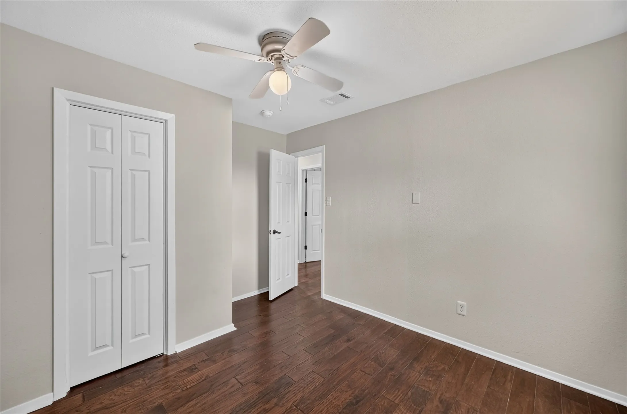 Second bedroom featuring rich wood-finish flooring, light neutral wall paint, and white baseboards