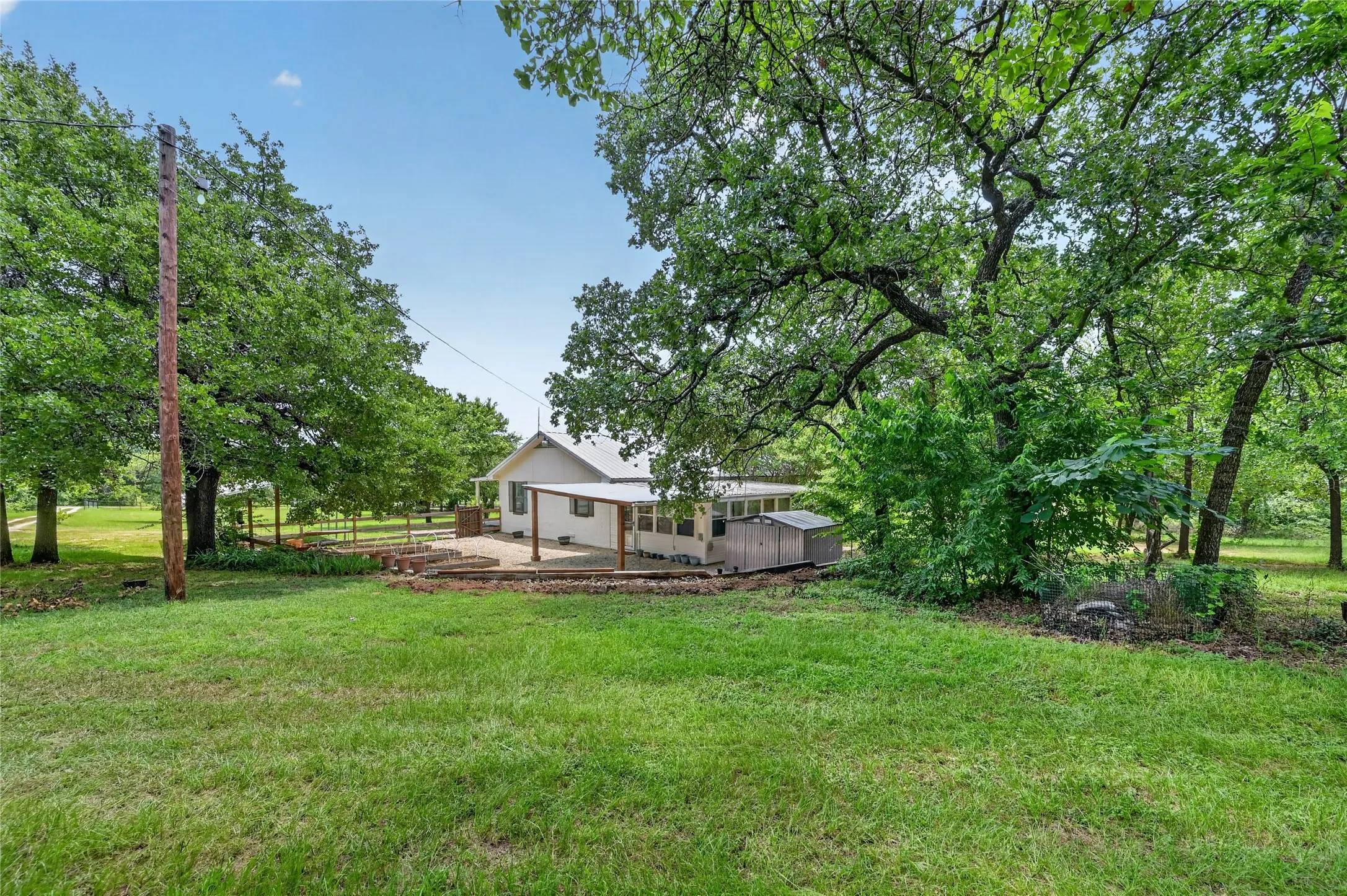 Expansive green lawn surrounds a white-sided residence with a covered patio and storage shed