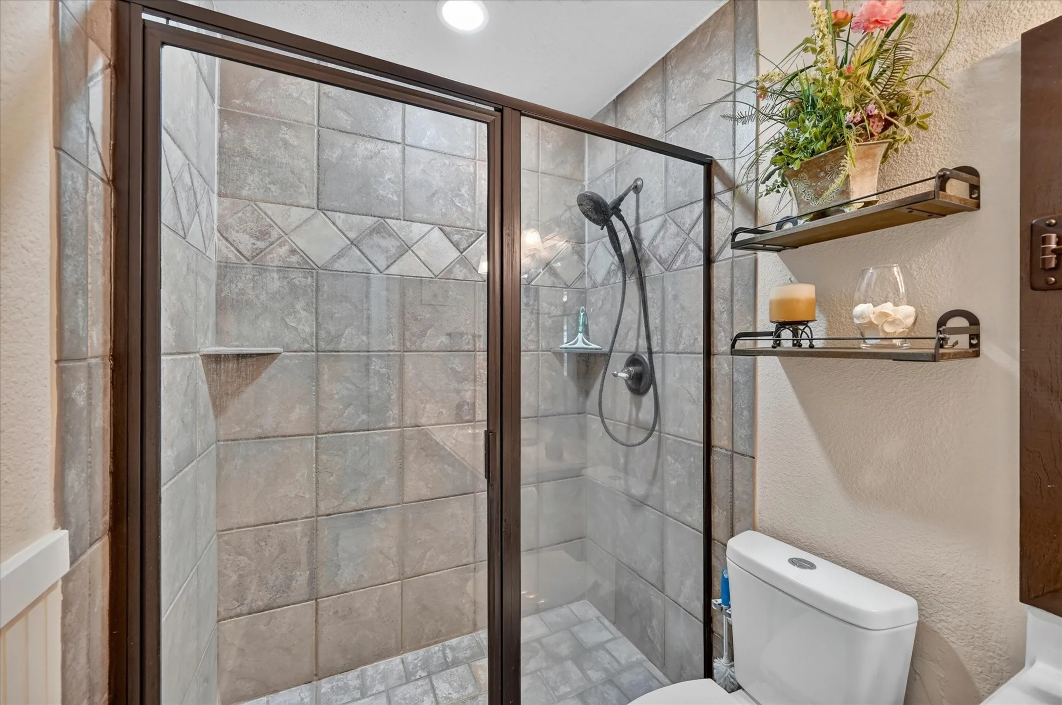 Walk-in shower featuring a glass enclosure with a dark bronze frame, full tile surround, integrated corner shelf, and a dark bronze shower fixture
