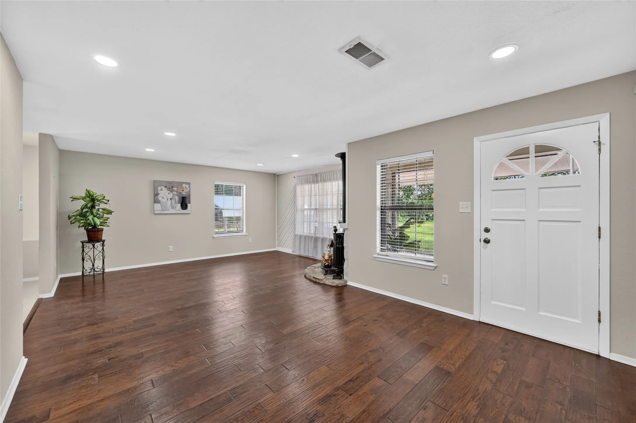 Spacious living area featuring rich wood-finish flooring, recessed lighting, and a white paneled entry door with an arched window