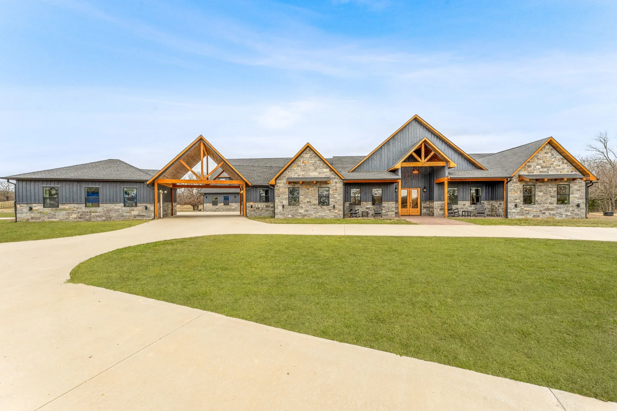 Modern farmhouse style home with stone siding, a front lawn, board and batten siding, and curved driveway