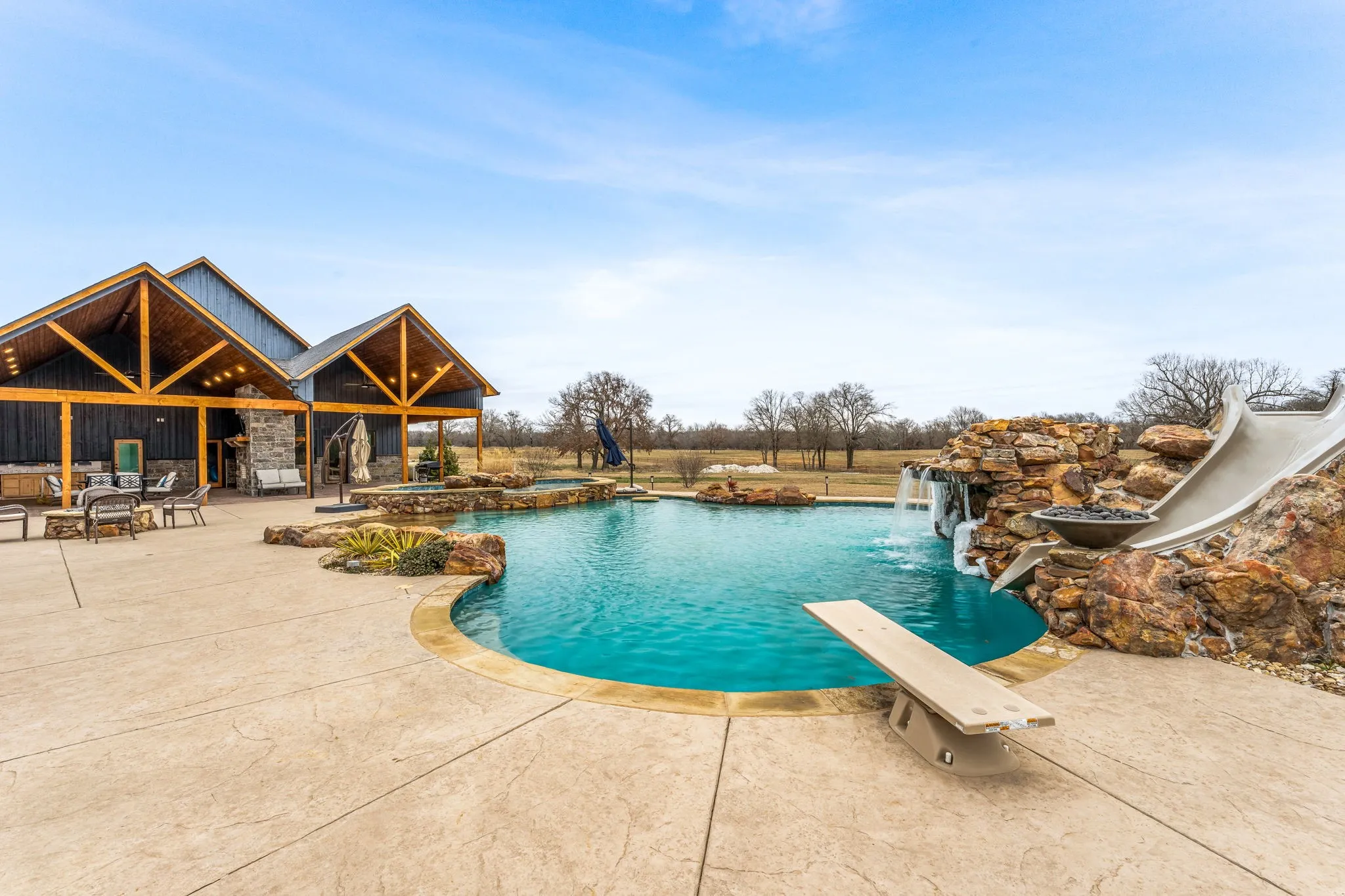 View of pool with a patio area, a diving board, a water slide, and a pool with connected hot tub