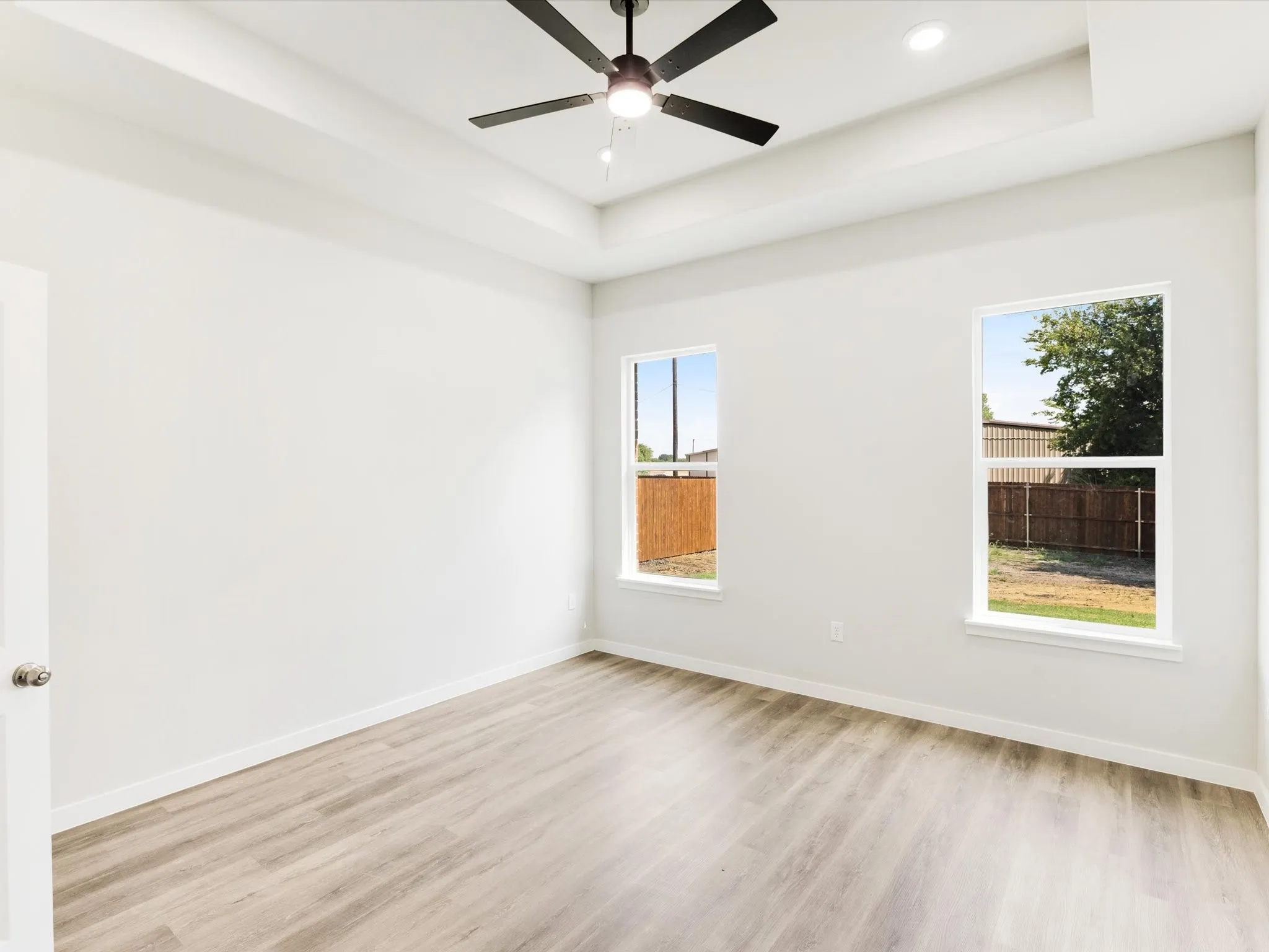 Tray ceiling, recessed lighting, ceiling fan, wood-finish flooring, and two windows